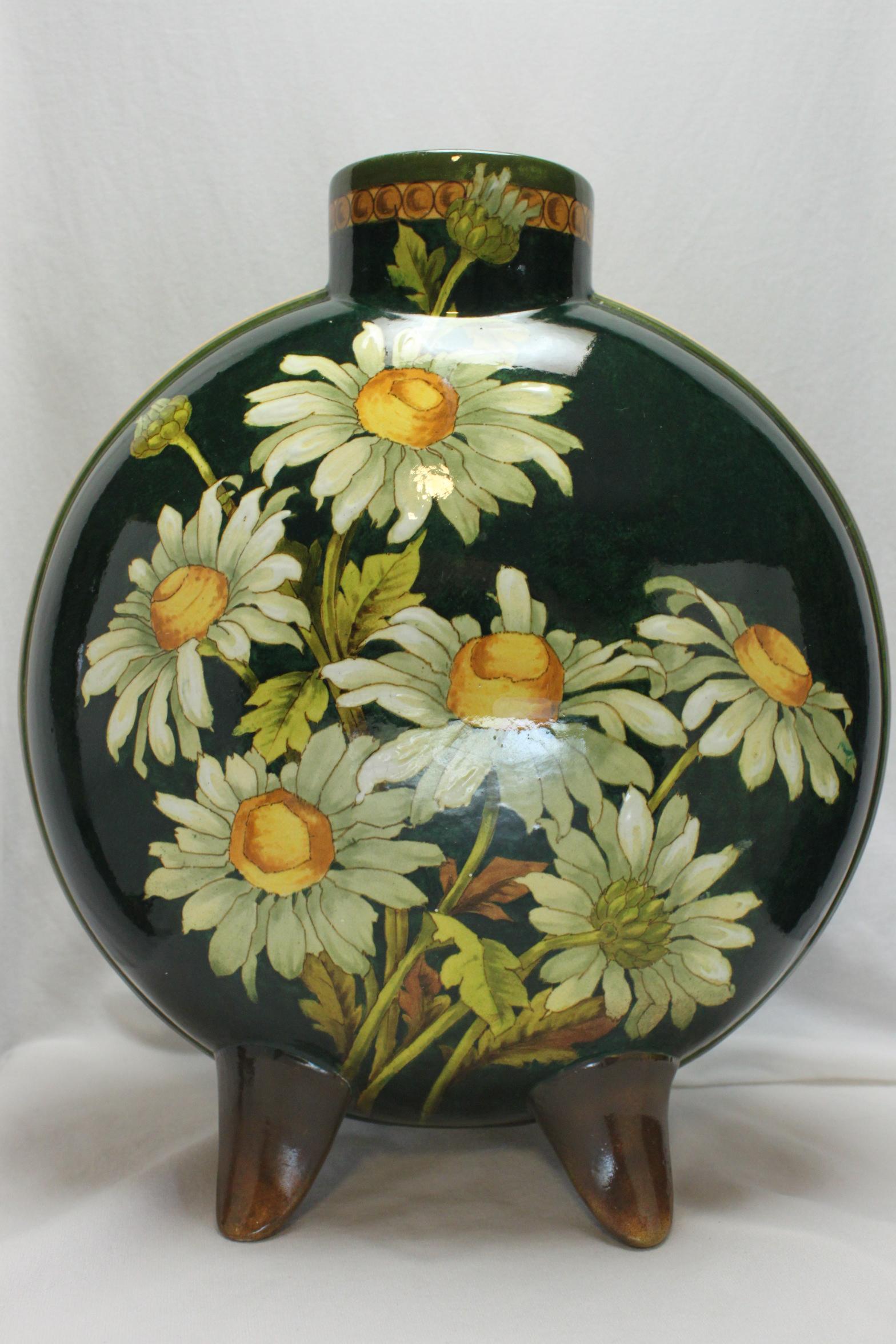 Decorated in the taste of the Aesthetic Movement, this Doulton Lambeth hand painted flask vase features an exuberance of flowers. On one side, a large spray of daisies sits on a dark green ground, whilst on the other, sunflowers peek out from a