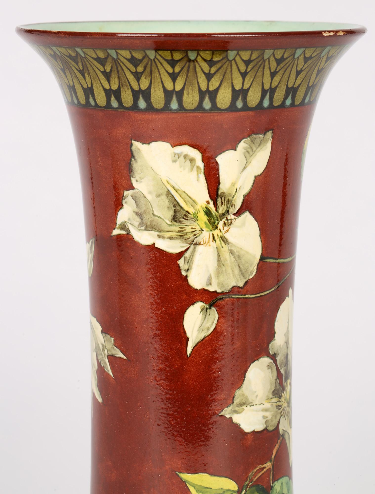 An exquisitely hand painted Doulton Lambeth Faience art pottery vase with trailing flowering stems by Helen A Harding and dating between 1877 and 1884. The tall elegant rounded cylindrical bodied vase has a wide rounded skirted base with a trumpet