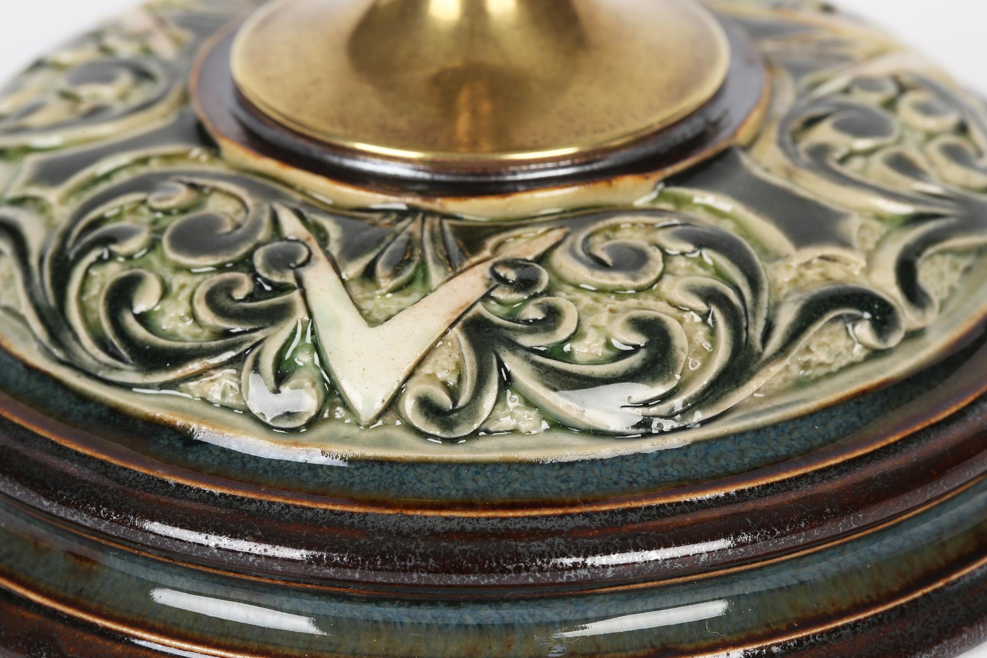 An unusual Doulton Lambeth saucer shape stylized leaf design candlestick with brass fittings by Frank Butler and dating from around 1890. The candle stick stands mounted on a wide rounded stoneware base with a shaped rim and moulded with V shaped