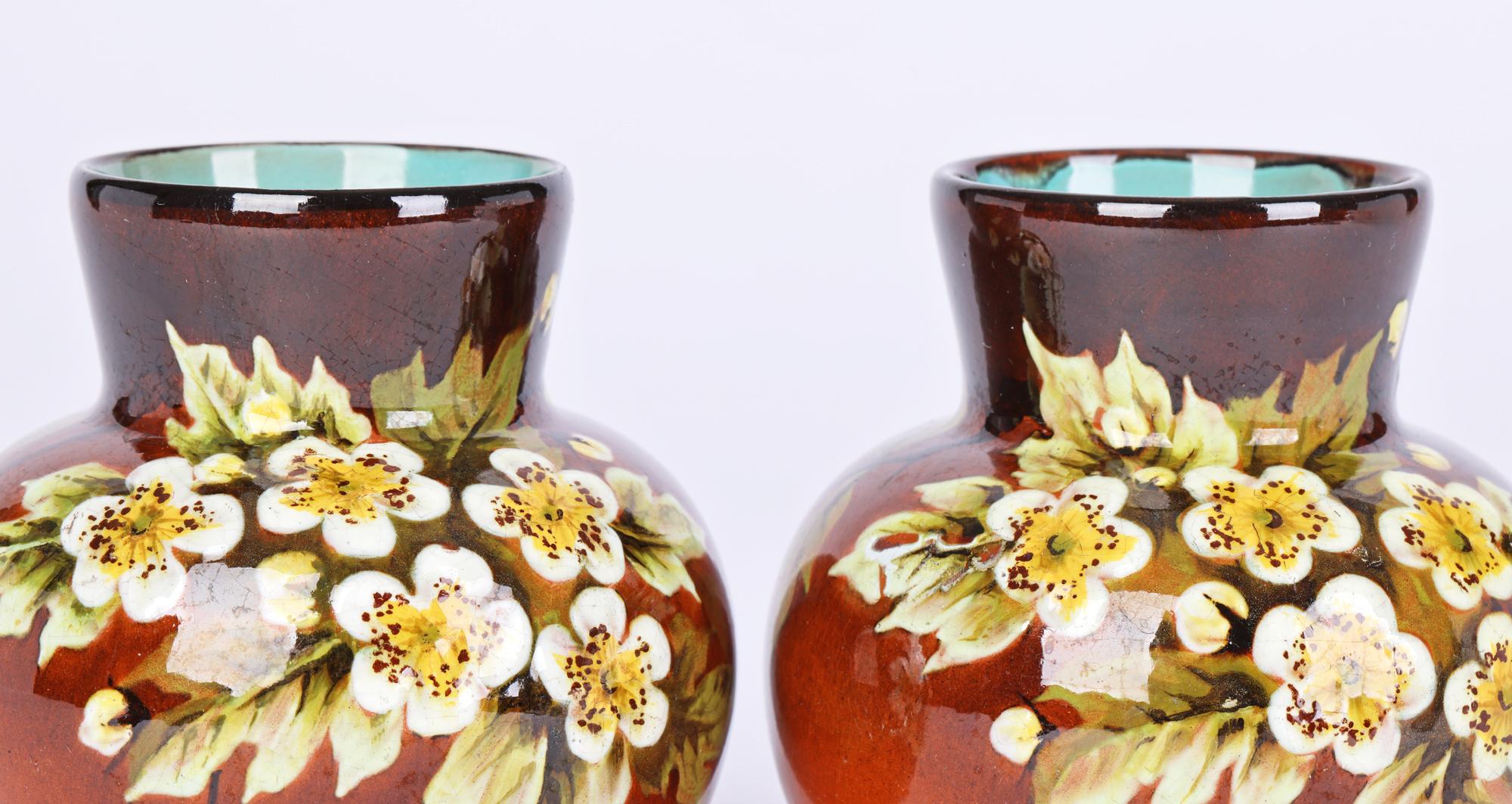 A stunning pair Doulton Lambeth Faience Impasto hand painted floral vases by Miss L Rogers and dating from around 1895. The red stoneware vase stand on a narrow unglazed foot with a slightly recessed base and are of squat round shape with a short