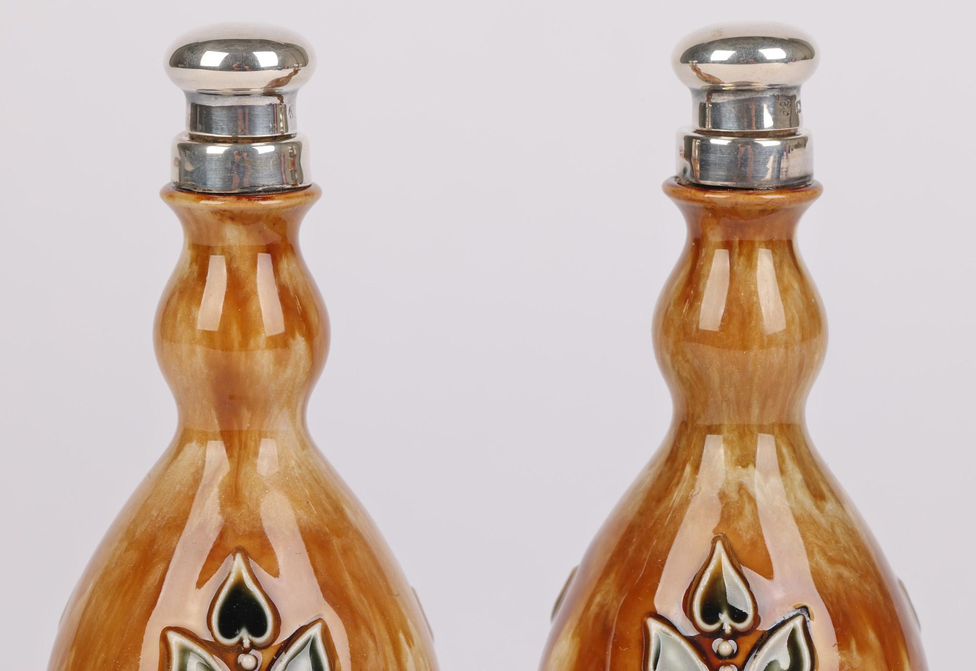 A very rare pair Doulton Lambeth silver mounted rose water flasks decorated with Art Nouveau styled floral designs by Miss O Heath and Winnie Bowstead and dating from 1920. The stunning pair stone ware bottle shaped flasks stand on flat round
