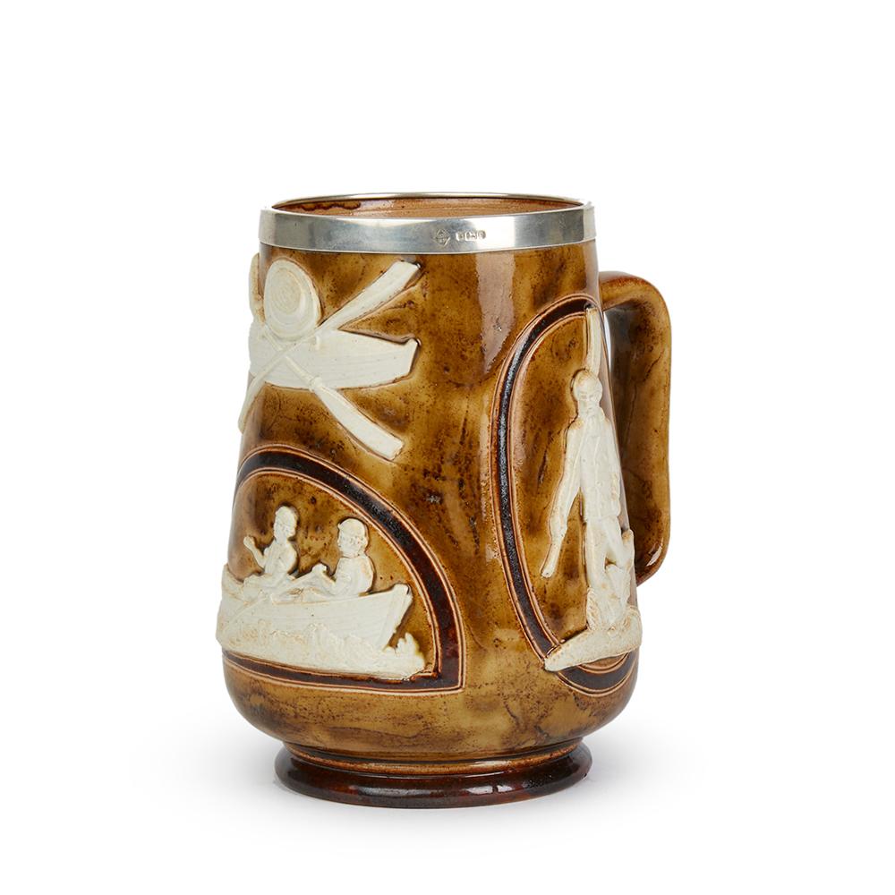 A rare antique Doulton Lambeth sporting tankard with white relief figures set against a brown salt glazed ground with a silver rim applied to the top edge. The stoneware tankard has impressed makers marks along with incised artist marks RH for