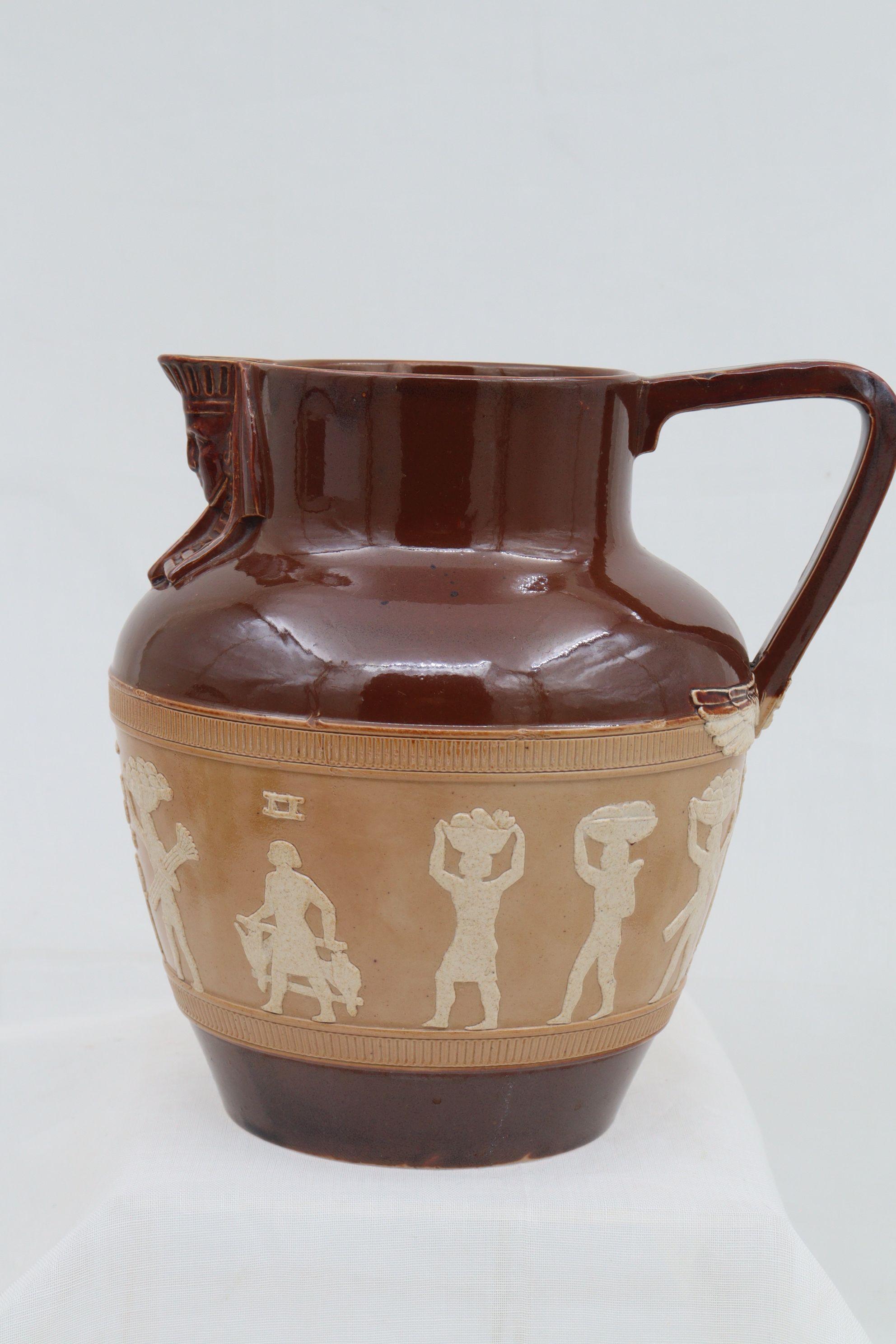 A very attractive salt glazed stoneware jug or pitcher from the Doulton Lambeth factory. It is decorated with a rather uncommon Egyptian theme. A pharaoh's head forms the spout and the wings of Horus spread either side of the base of the handle.