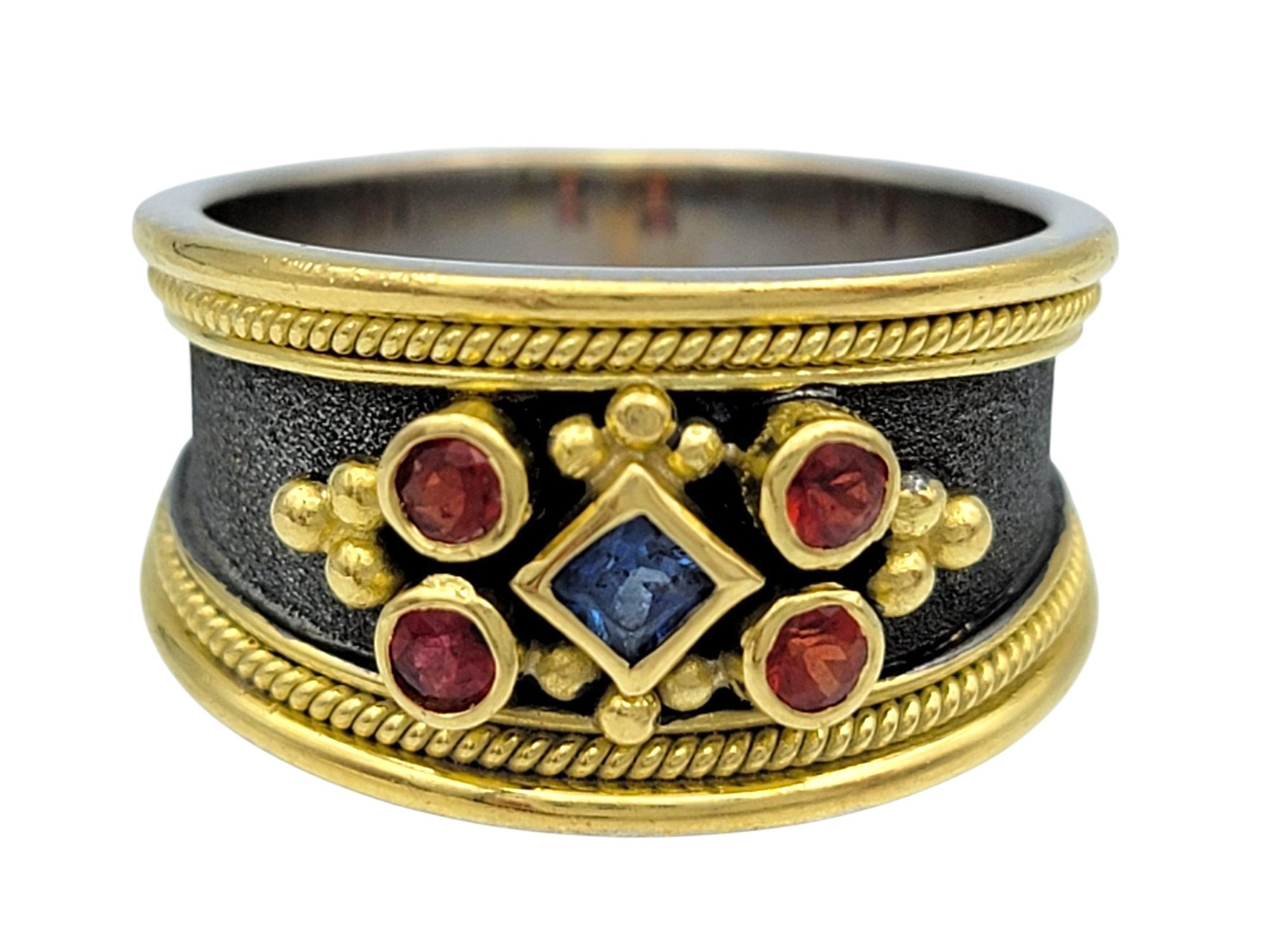 Misura dell'anello: 7 

Questo sorprendente anello con più zaffiri di Dovris è realizzato in oro giallo 18 carati e presenta uno straordinario intarsio in platino nero che aggiunge profondità e contrasto al design. Un regale mix di zaffiri rossi e