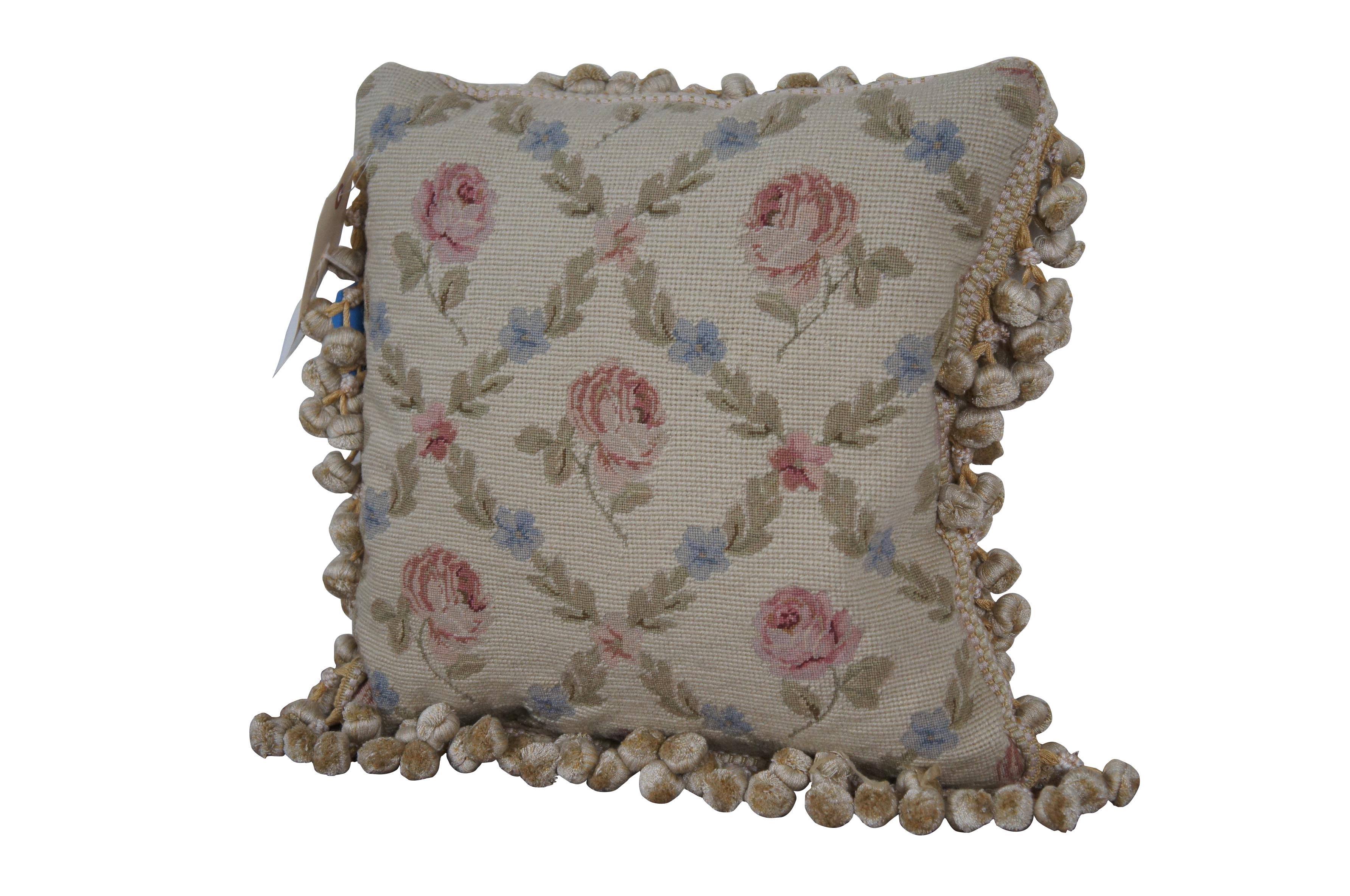 20th century square needlepoint throw pillow, hand embroidered with a pattern of pink roses, divided by criss crossing lines of pink and blue flowers and leaves, on a slightly yellow beige background. Cream and gold ball tassel trim. Cream velour
