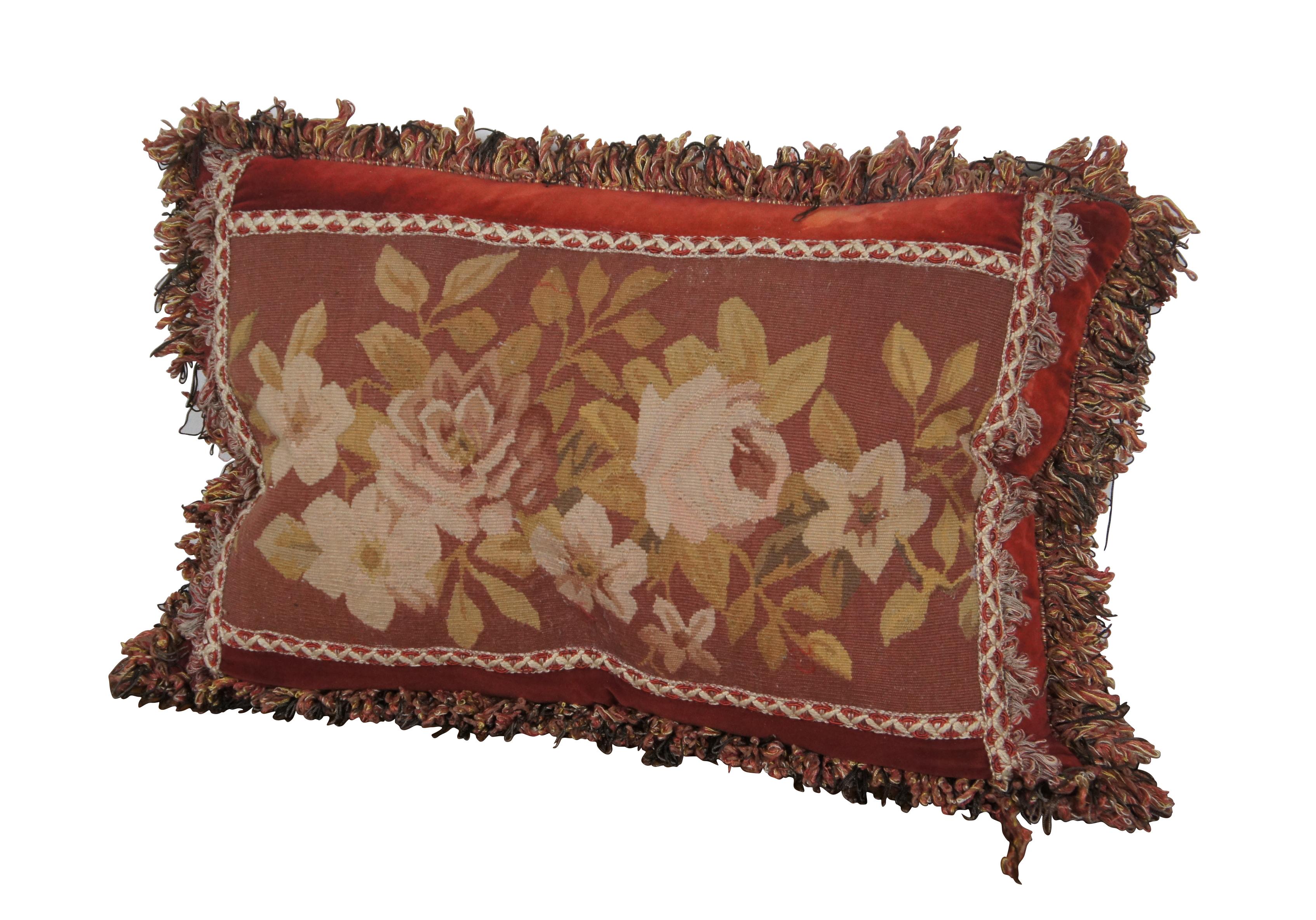 20th century rectangular lumbar / throw pillow, embroidered with an array of roses / flowers in rust red, pink, gold, and cream, framed in cream and red trim. Red, gold, and gray fringe. Red velvet / velour back with zipper closure. Down