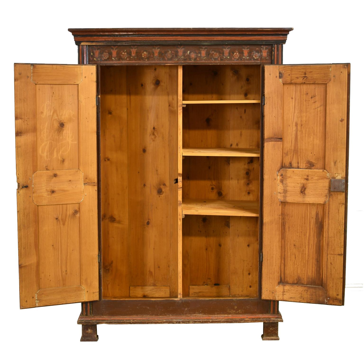 A beautiful wedding armoire featuring painted urns with floral bouquets on the red panels of the doors, with swags of flowers along the frieze and waist that are all stylized representations typical of folk art. Armoire has a painted maroon-color