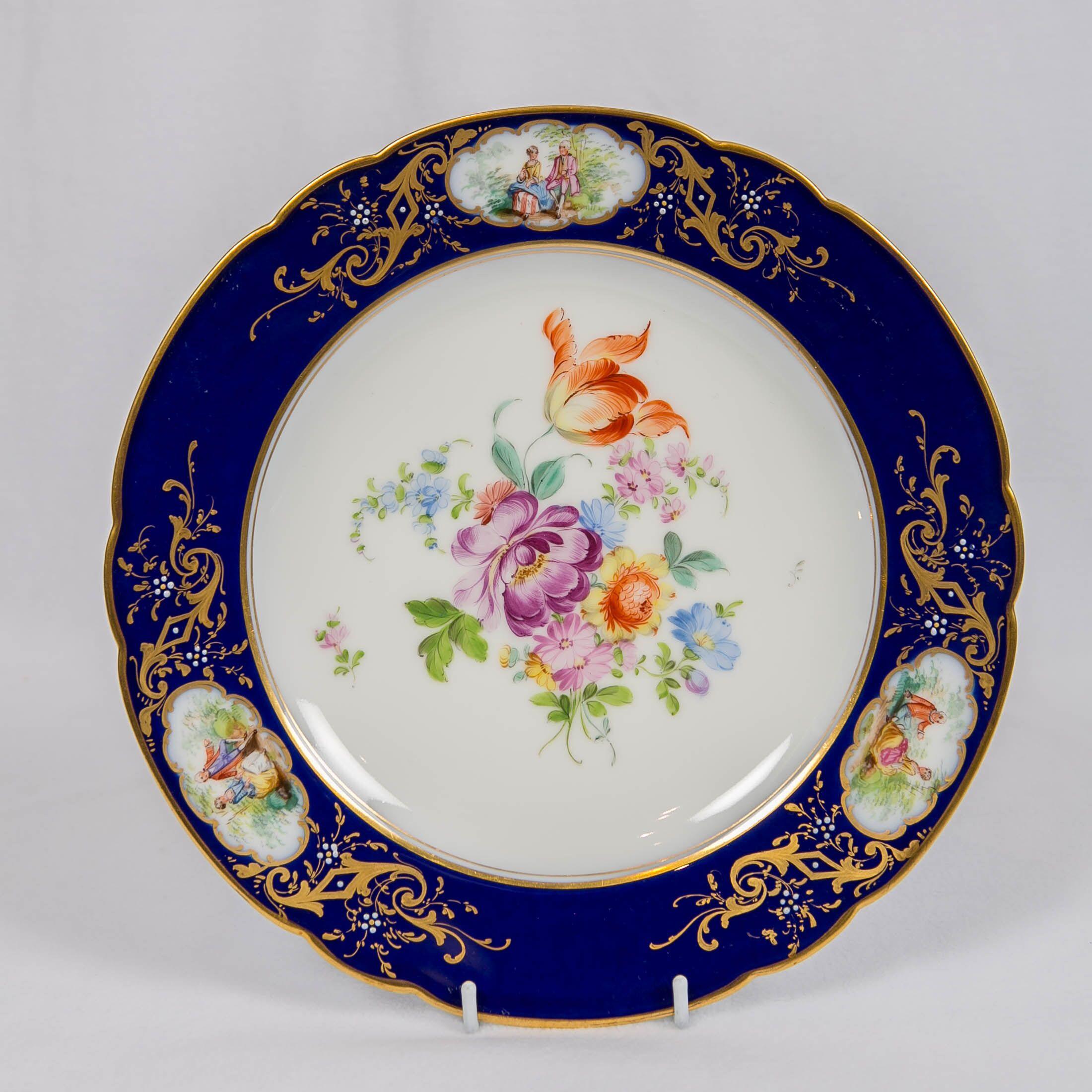 We are pleased to offer this set of a dozen Dresden China dinner dishes with a beautiful, large bouquet of colorful flowers in the center, encircled by deep blue borders decorated with scrolling gilt and three cartouches showing romantic