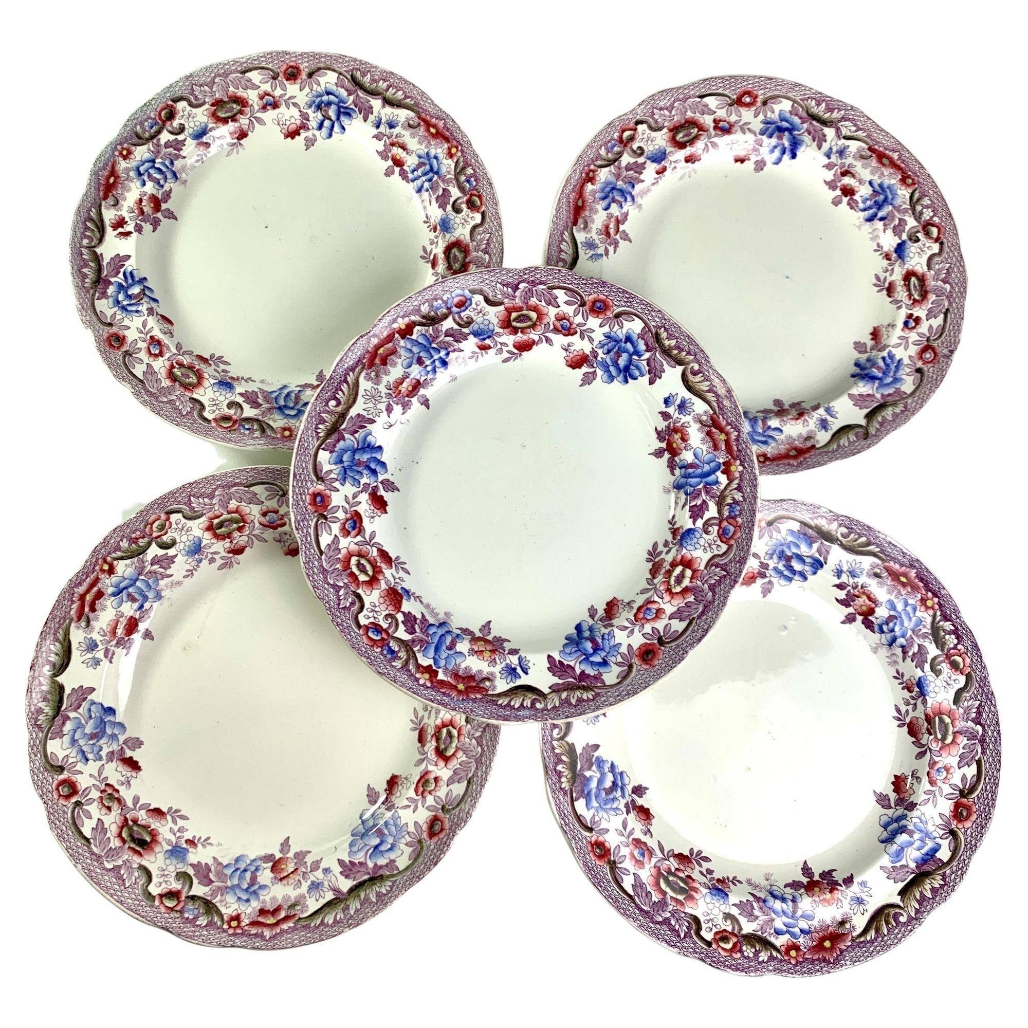 This set of a dozen antique earthenware dishes has beautiful borders filled with flowers painted in dusty purple and light blue, some with pale yellow centers and purple leaves.
Close to the edge of the dish, we see a pattern of purple darts.
The