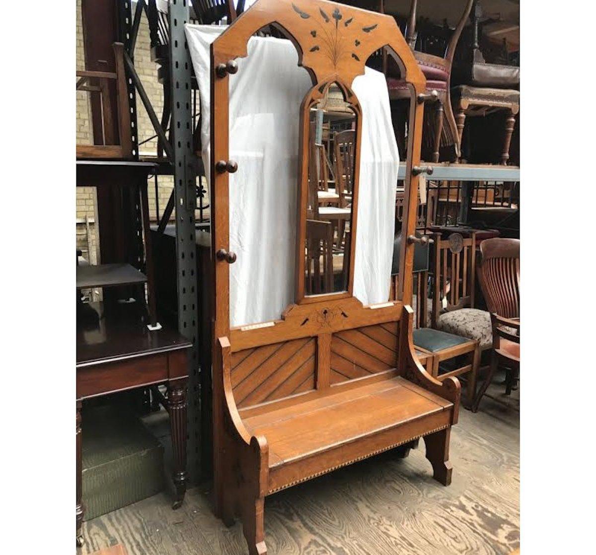 Dr C. Dresser style of, An Aesthetic Movement Gothic style oak hall stand with central arched mirror, flanked by open sides and six turned button ended coat hooks to the outer edges, with mitred plank details above a lift up seat with storage below,