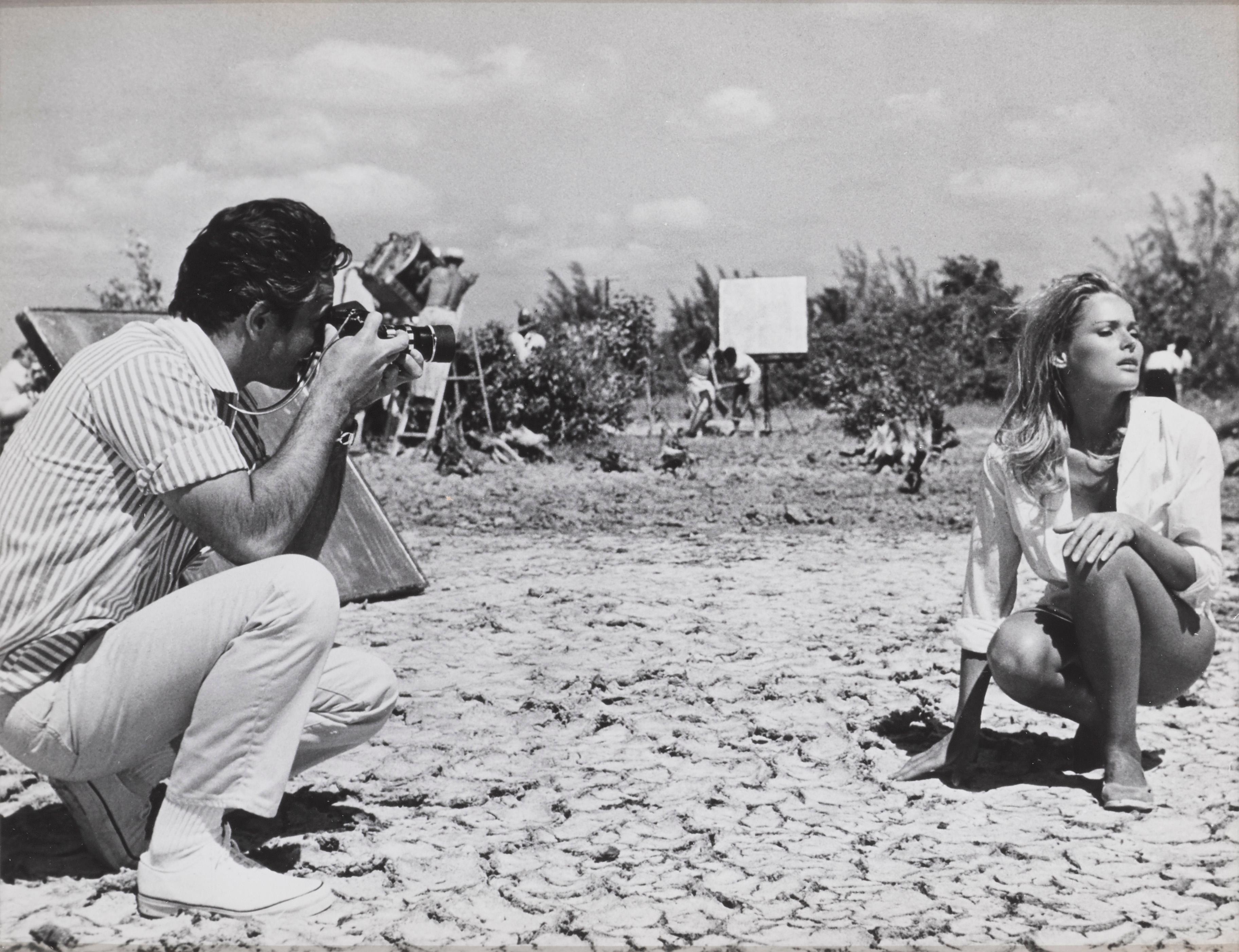 Original candid photographic production still showing Ursula Andress's husband John Derek taking a photograph of her on the set of Dr. No.\N- Original candid photographic production still showing Ursula Andress's husband John Derek taking a