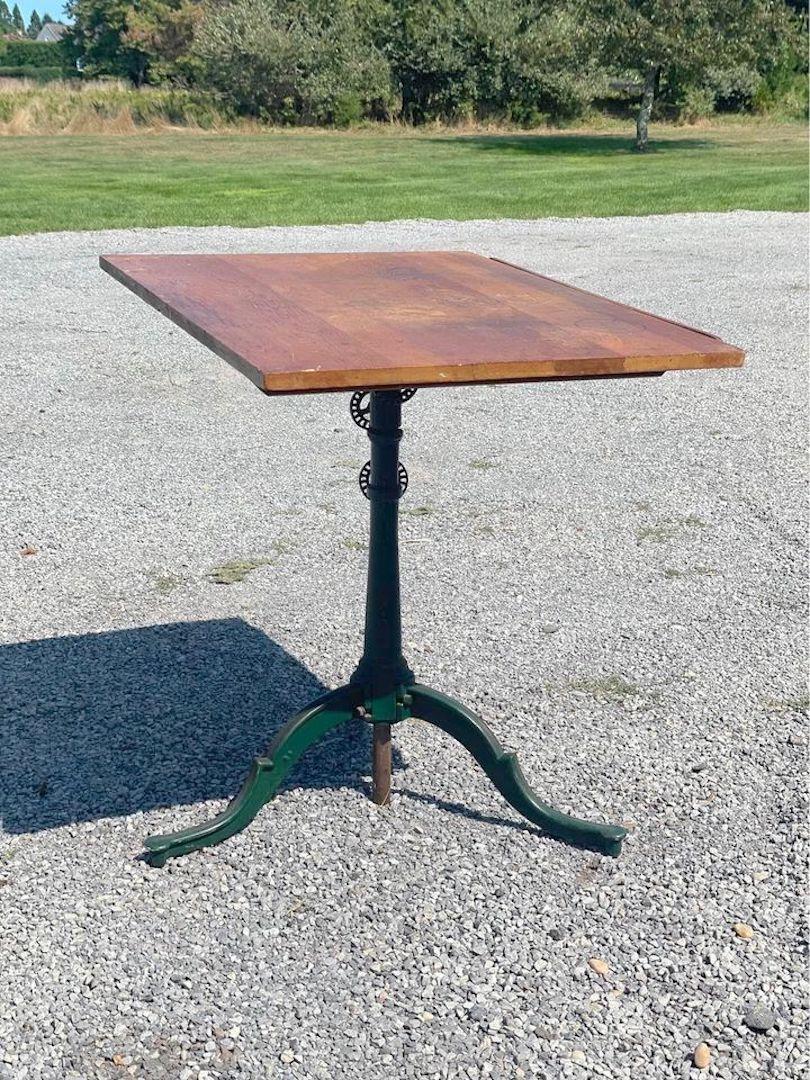 The drafting table is antique cast iron tripod leg with wood tilt top. Adjustable height and angle and has paper holder. The antique table was made by Anderson company in Brooklyn, New York. The industrial table top measures 31