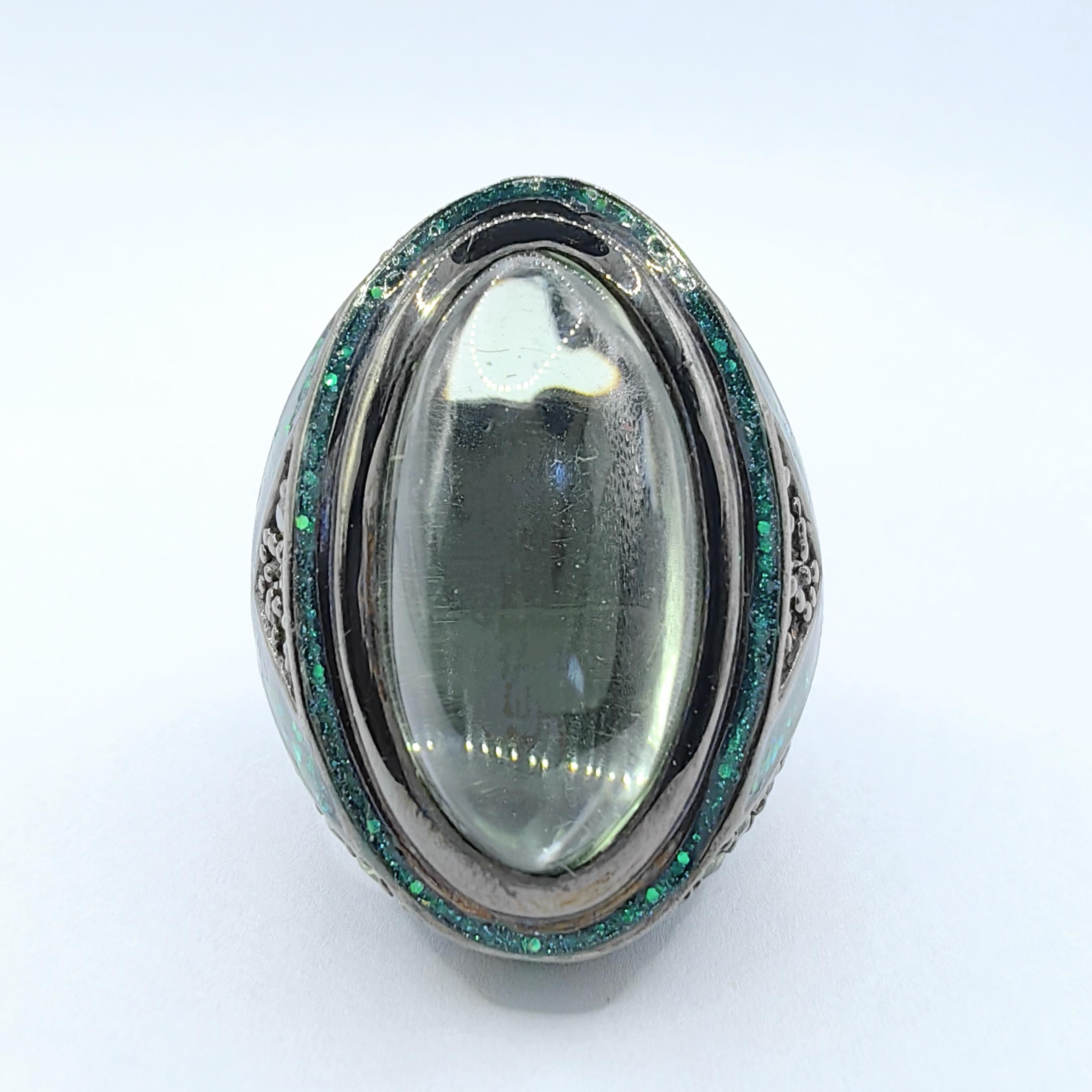Lassen Sie sich von der mystischen Anziehungskraft des Dragon Eye Green Amethyst & Sapphire Cocktail Statement Rings aus Sterlingsilber verzaubern. Ein außergewöhnliches Stück, das Kühnheit und den Glanz der Natur verkörpert. Das Herzstück ist ein