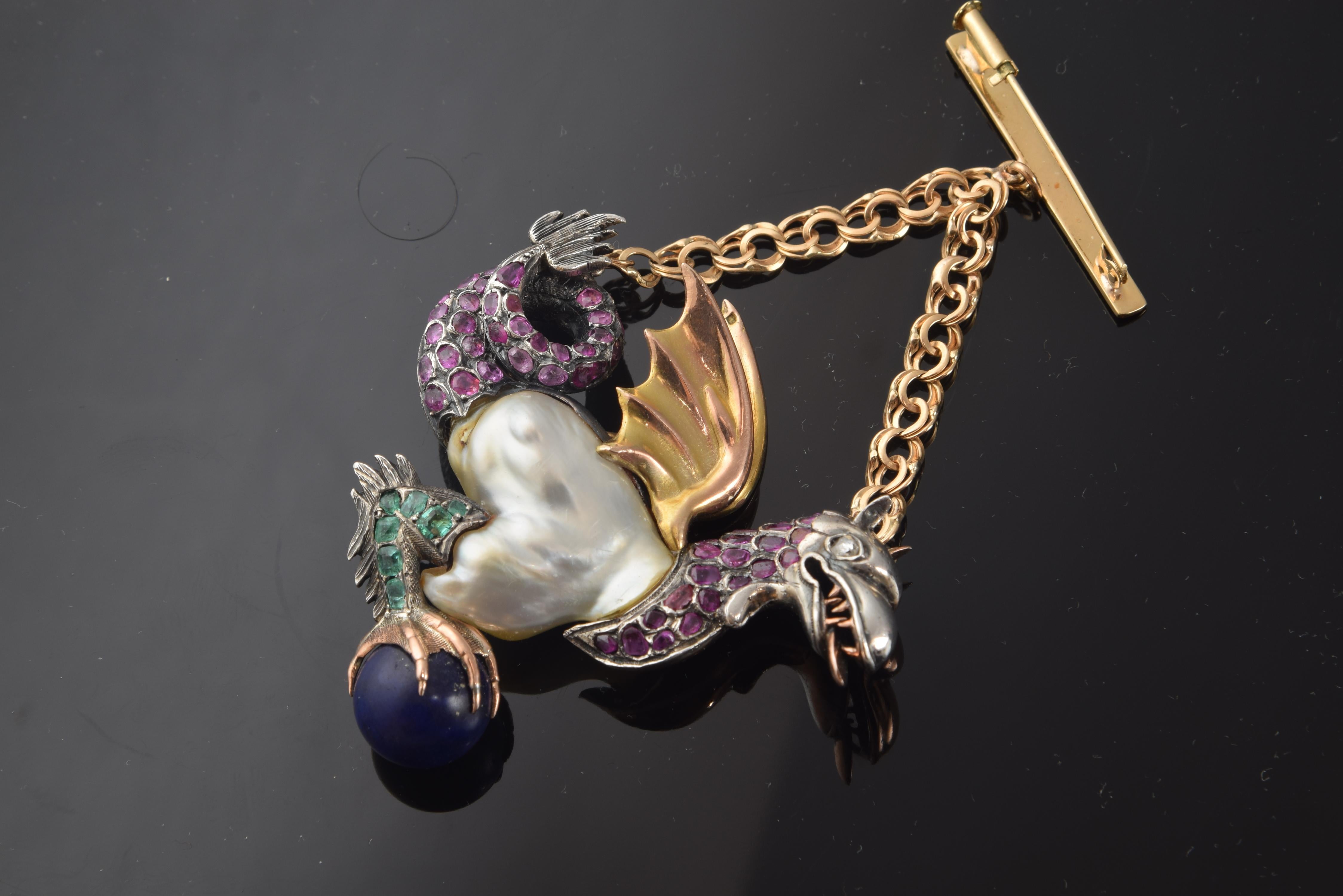 A chain attached to the dragon's head and tail keeps the brooch in its correct position. This one represents a dragon, with its tail curled and a Baroque pearl under its overwrought wings, making the body of the animal; He holds a blue sphere on his