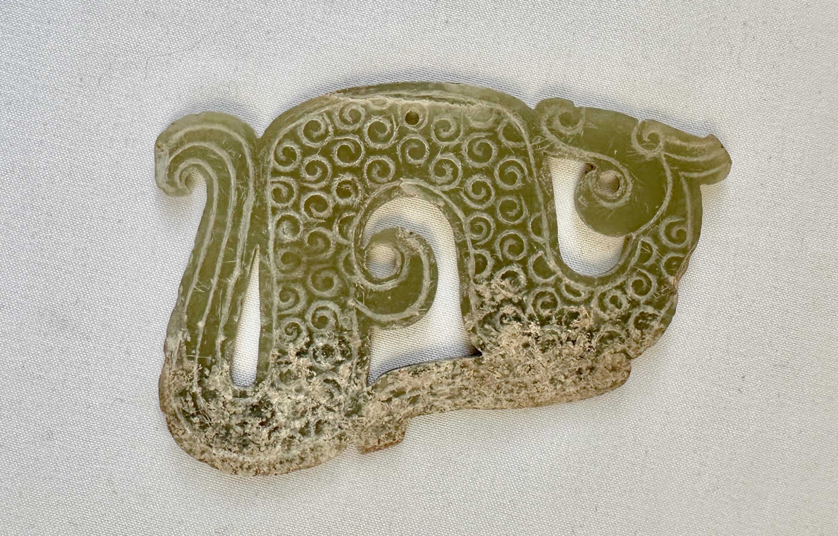 Celadon green jade dragon-shaped pendant, Eastern Zhou Dynasty (770 - 221 B.C.E.). 

Worked in the form of a sinuous dragon with its head turned towards an upturned tail, the body carved on both sides in low relief with slightly raised spirals or