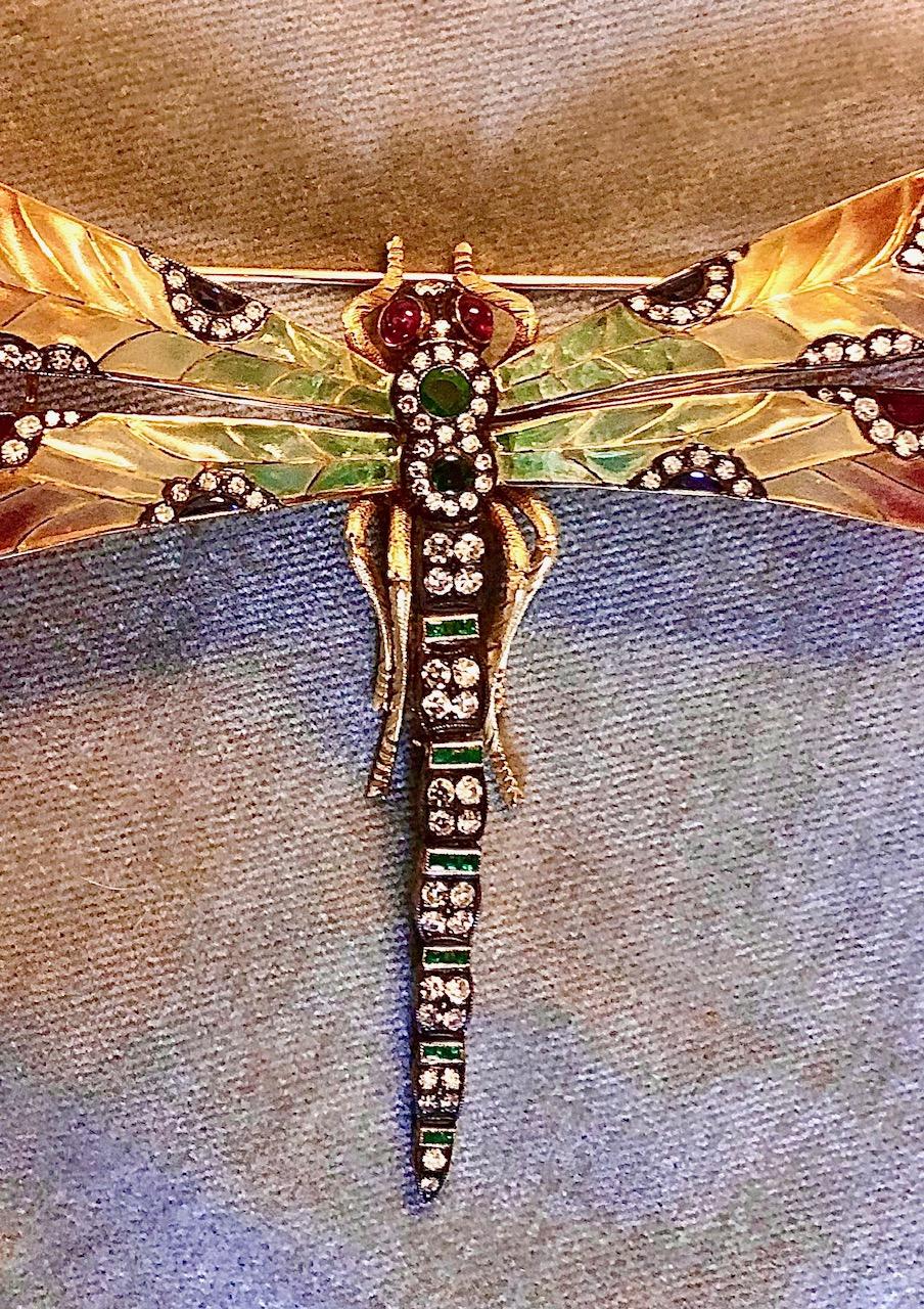 Dies ist eine wirklich spektakuläre Brosche. Aus 18-karätigem Gold und Silber, besetzt mit Rubinen, blauen Saphiren, Smaragden, Demantoid-Granaten und funkelnden Diamanten im Einzelschliff.

Die Form ist die einer großen Libelle mit wunderschöner