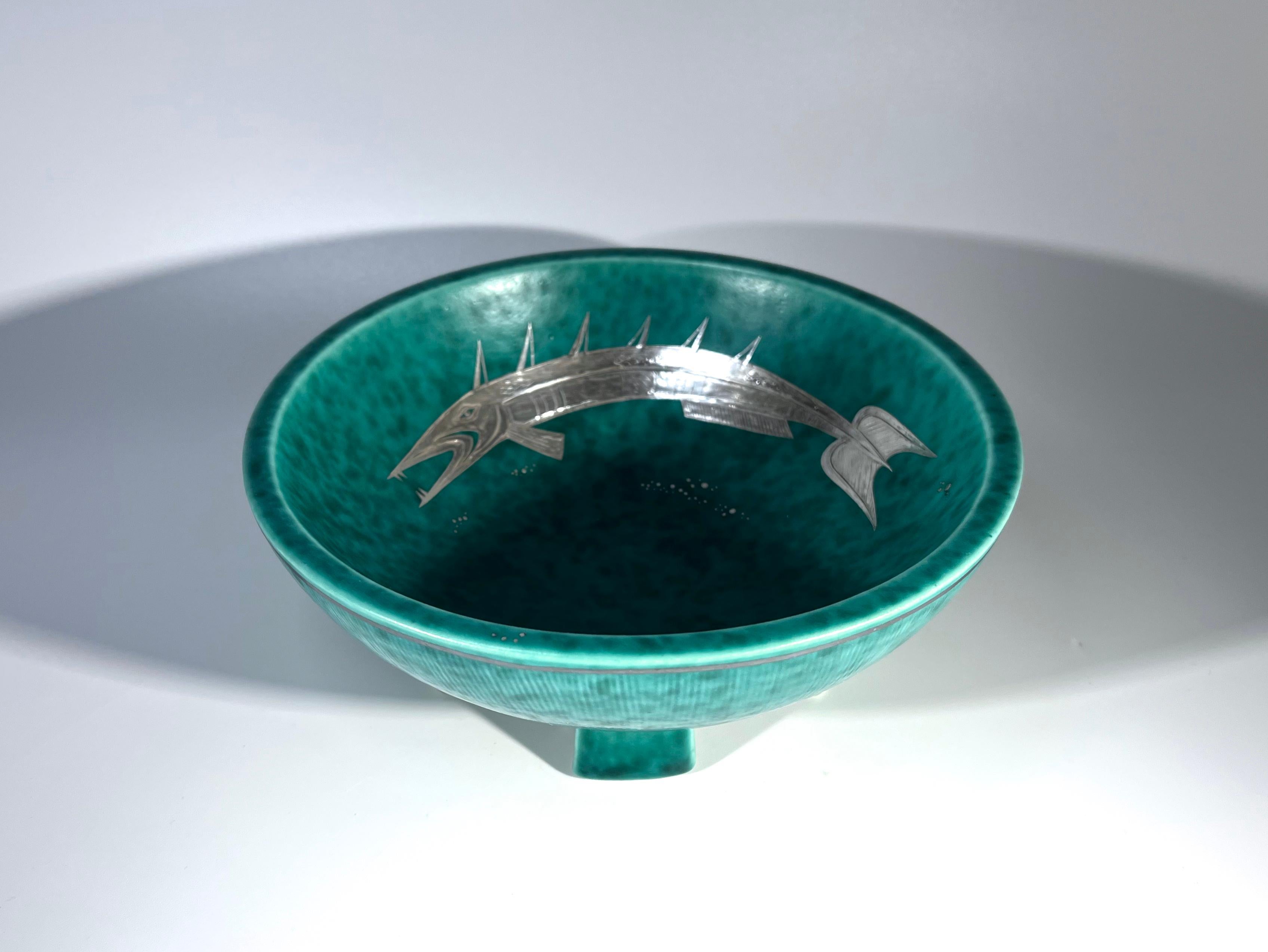An extravagant Argenta stoneware, five legged fish bowl by Wilhelm Kage for Gustavsberg, Sweden 
A fascinating barbed fish of applied silver, decorates the interior of this tactile and dramatic piece
Circa 1932. Date letter B
Stamped Argenta A10 on