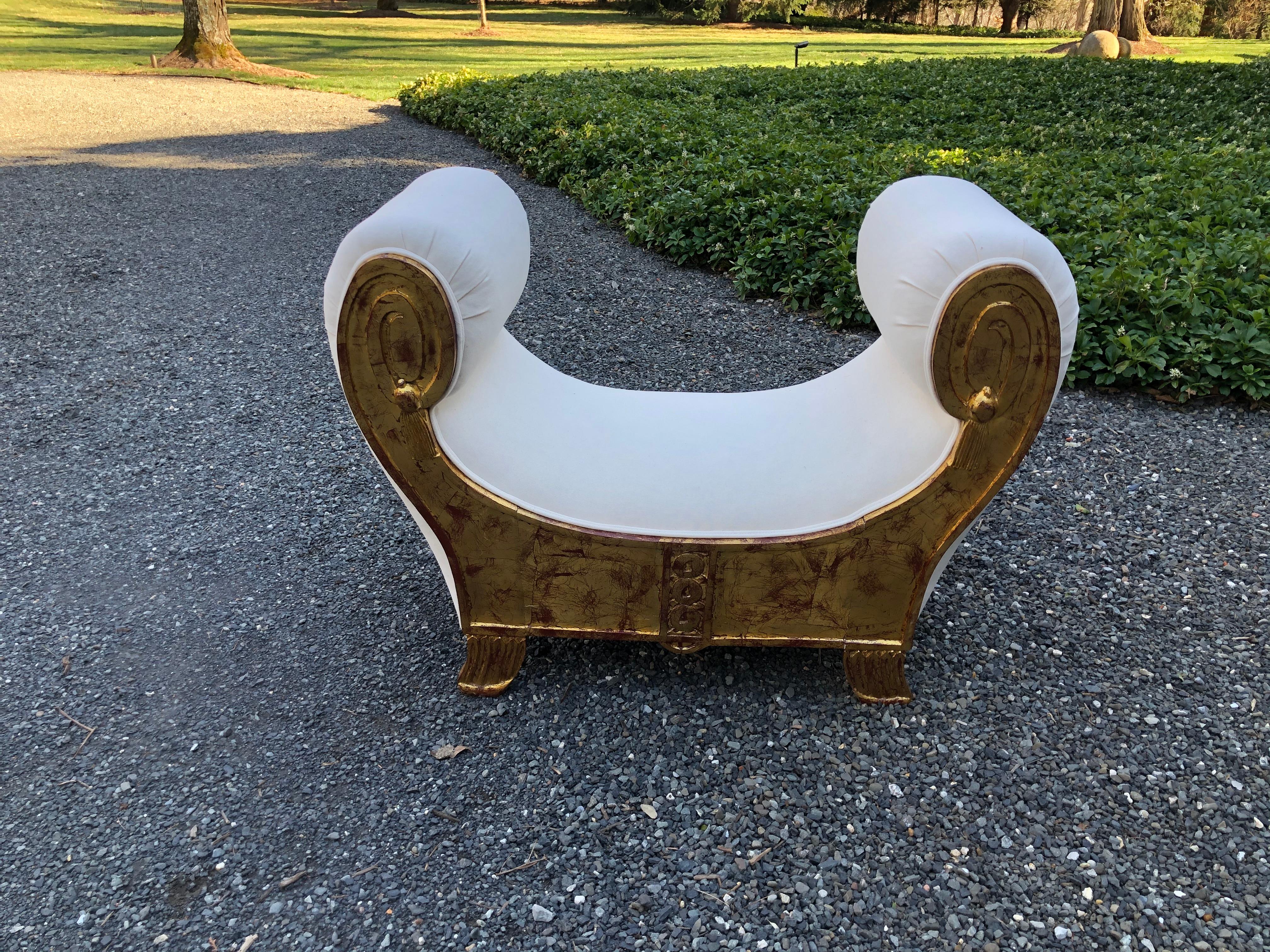 Elegant Egyptian Revival giltwood bench newly upholstered in crisp white cotton duck. The bench has beautiful patina with touches of red showing through the gold leaf and carved decoration on the feet, apron and arms.
 