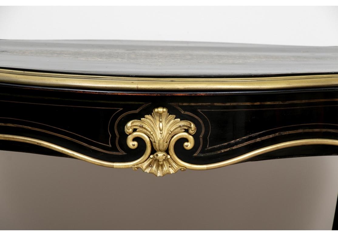 A very well made Console with a dramatic and Stately presence. A classic serpentine Napoleon III console table, ebonized with elaborate and fine dore details. The top with an inlaid serpentine brass medallion in the center having an almost Damascene