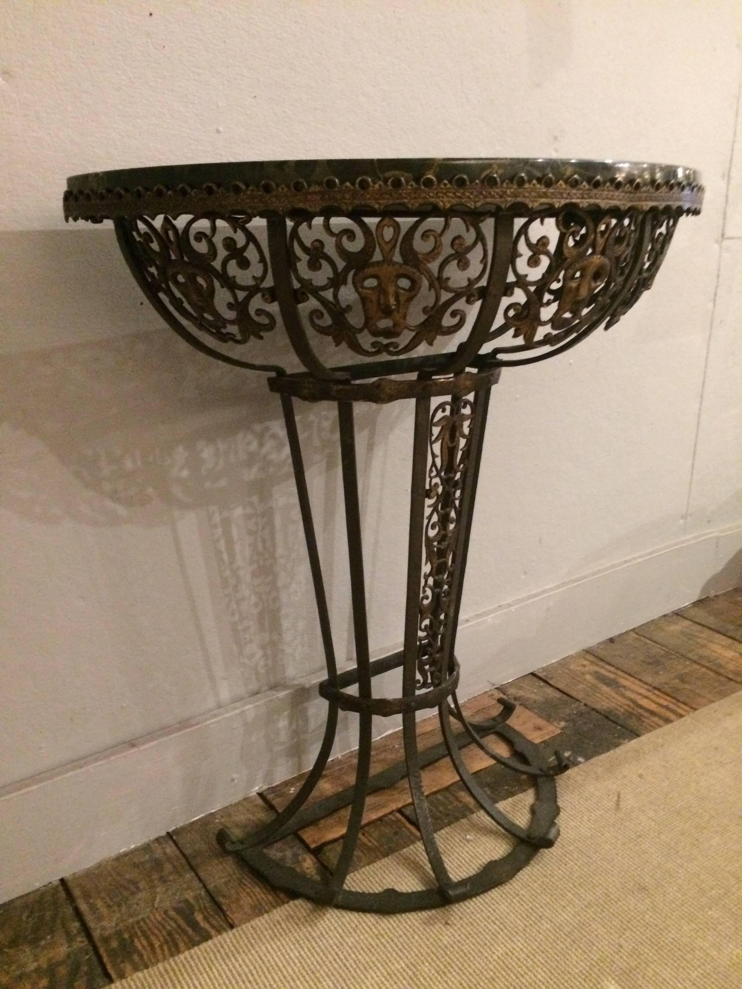 A striking demilune shaped console table having two-tone filligree iron work base with theatrical mask faces, leafy scroll work, and inset black marble top.
