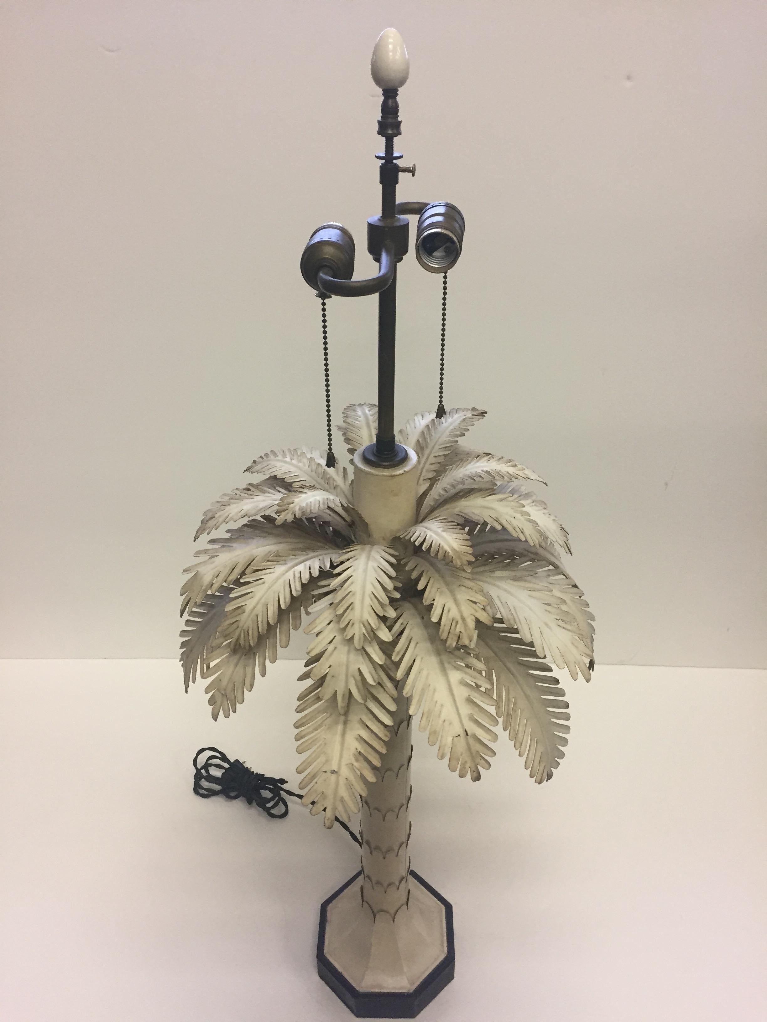 Glamorous tole table lamp painted cream having a mass of feathery palm leaves on top of a decorative tree trunky column.
2 60 watt sockets.
 