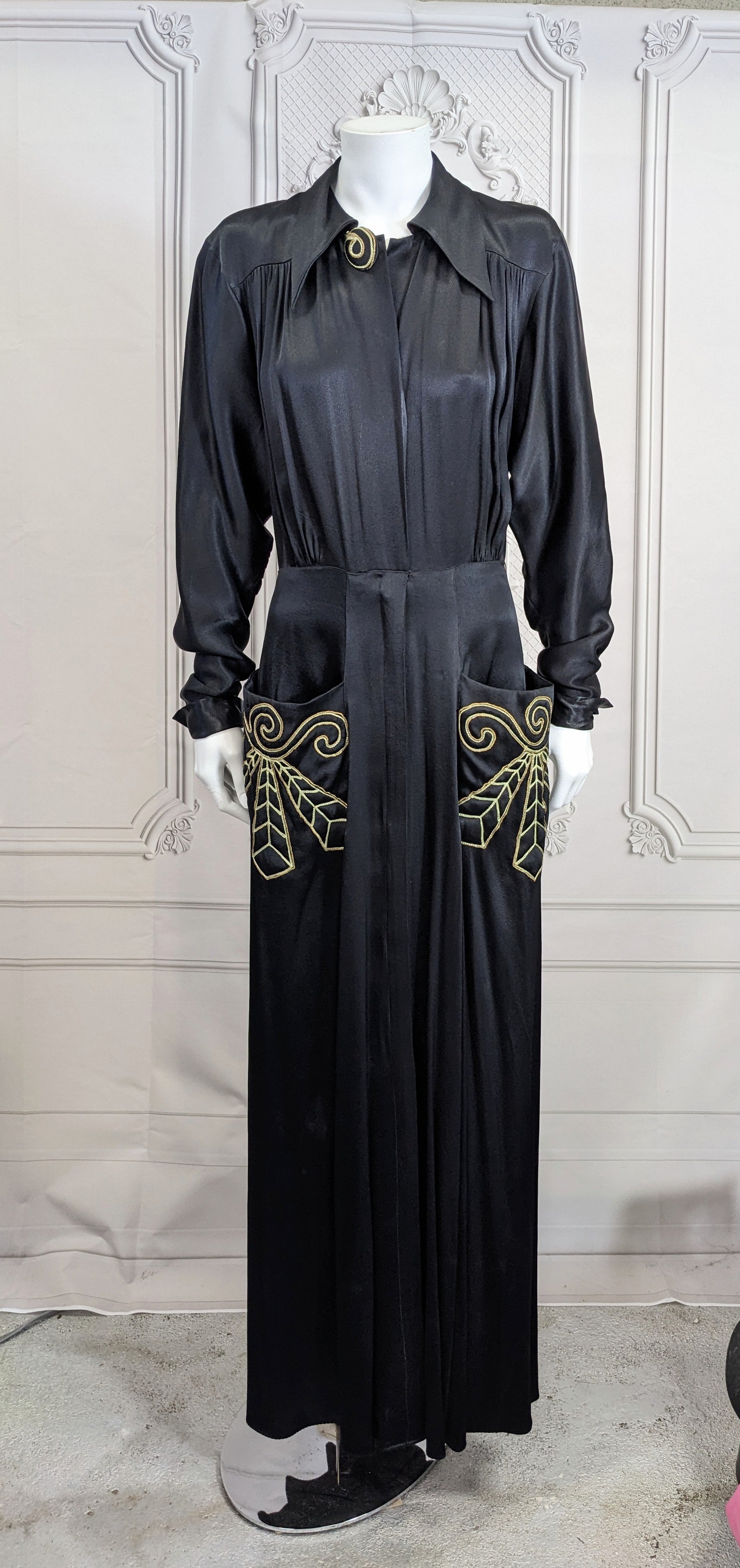 Dramatic Retro Silk Satin Embroidered Dressing Gown from the 1940's. Shirtwaist style in slinky black silk satin with Art Deco style soutache embroidery in yellow and gold tinsel on the stand away pockets and top button.
Designed as a home dressing