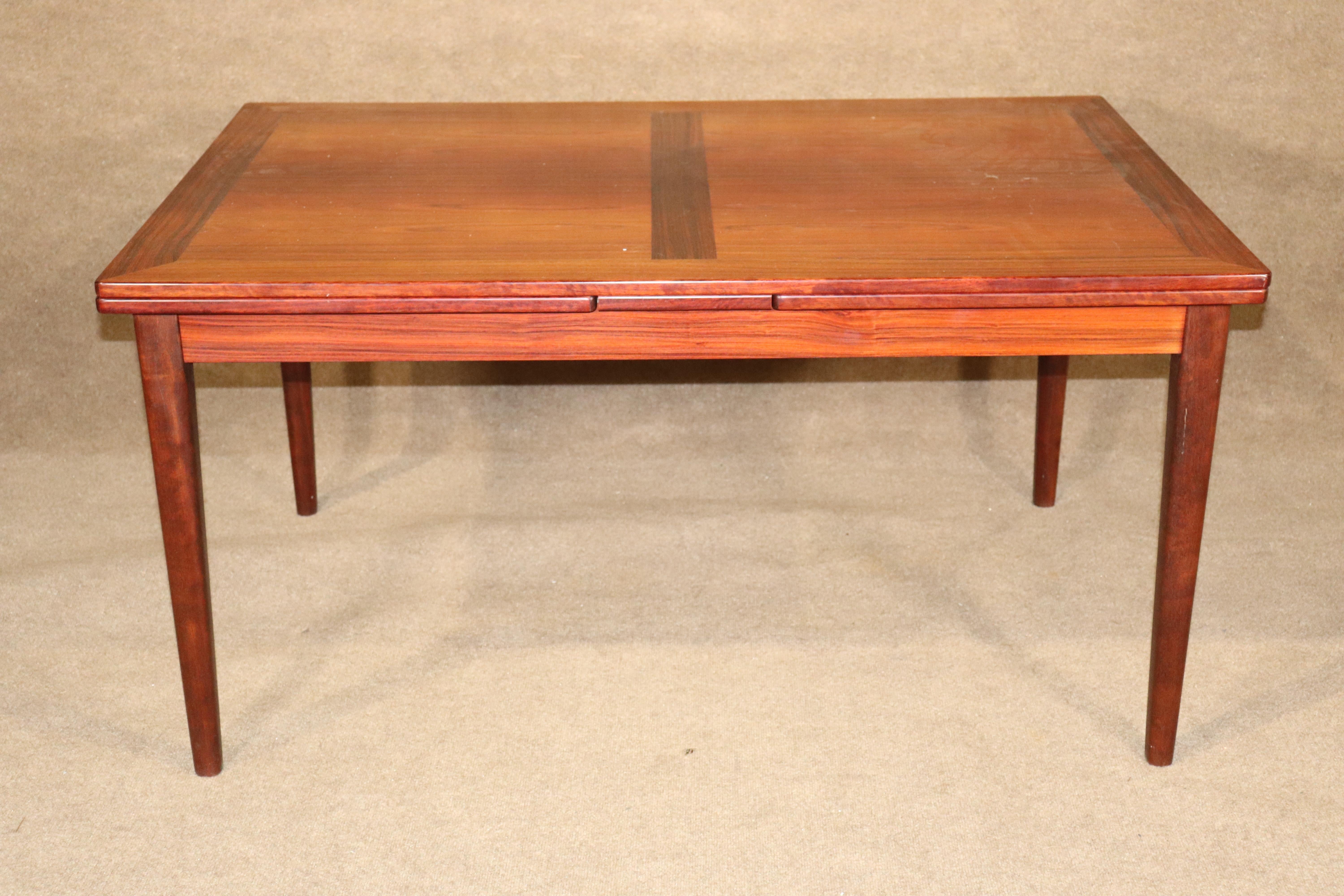 Danish made dining table in rich rosewood grain. Two leaves hide underneath the table top and are easily pulled out to extend the surface to 102