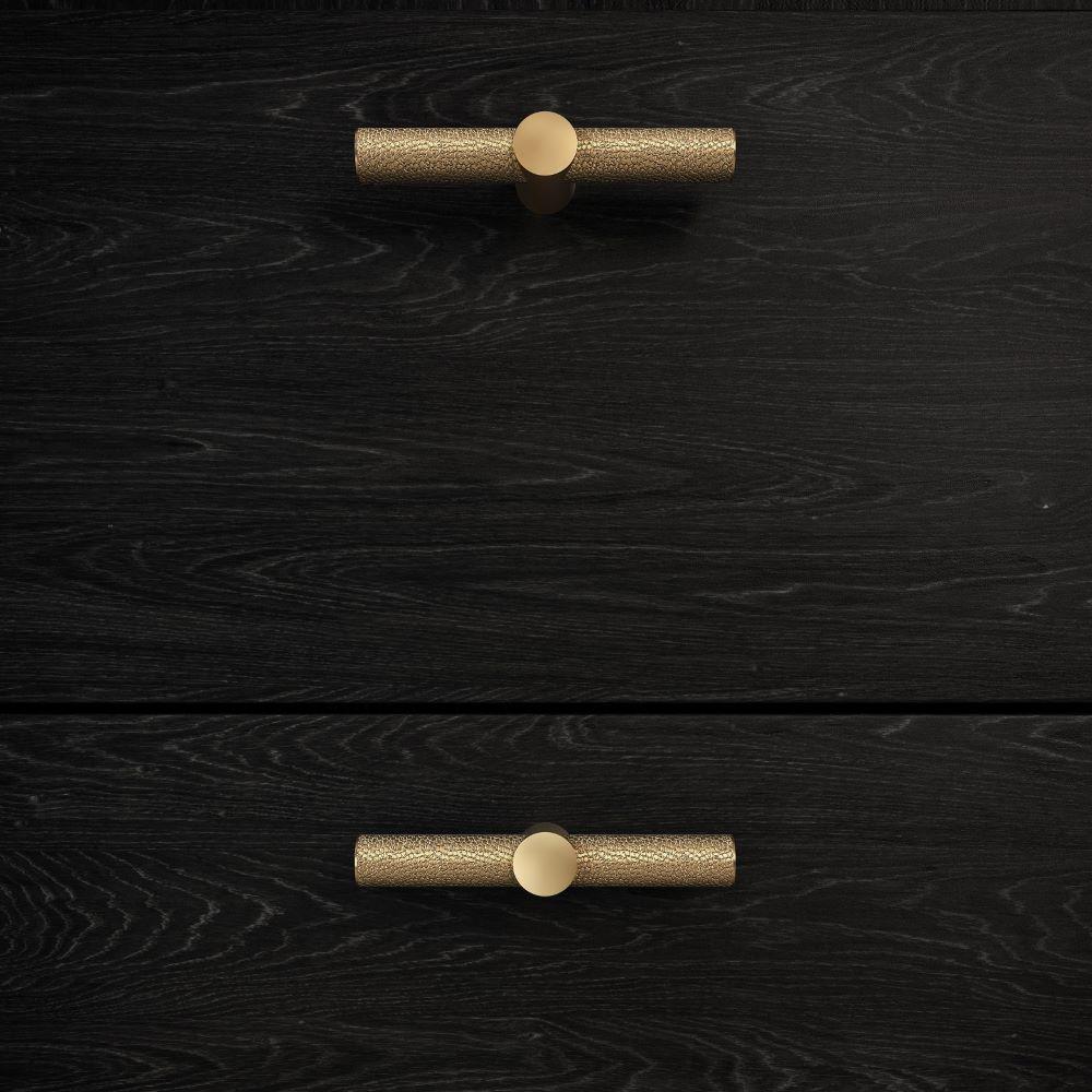 This 8 cm cabinet pull is crafted from solid brass and belongs to the Art Deco collection. Its tubular shape is refined, with proportions suited for smaller furniture fronts. The surface features a dense, hand-hammered pattern inspired by shagreen
