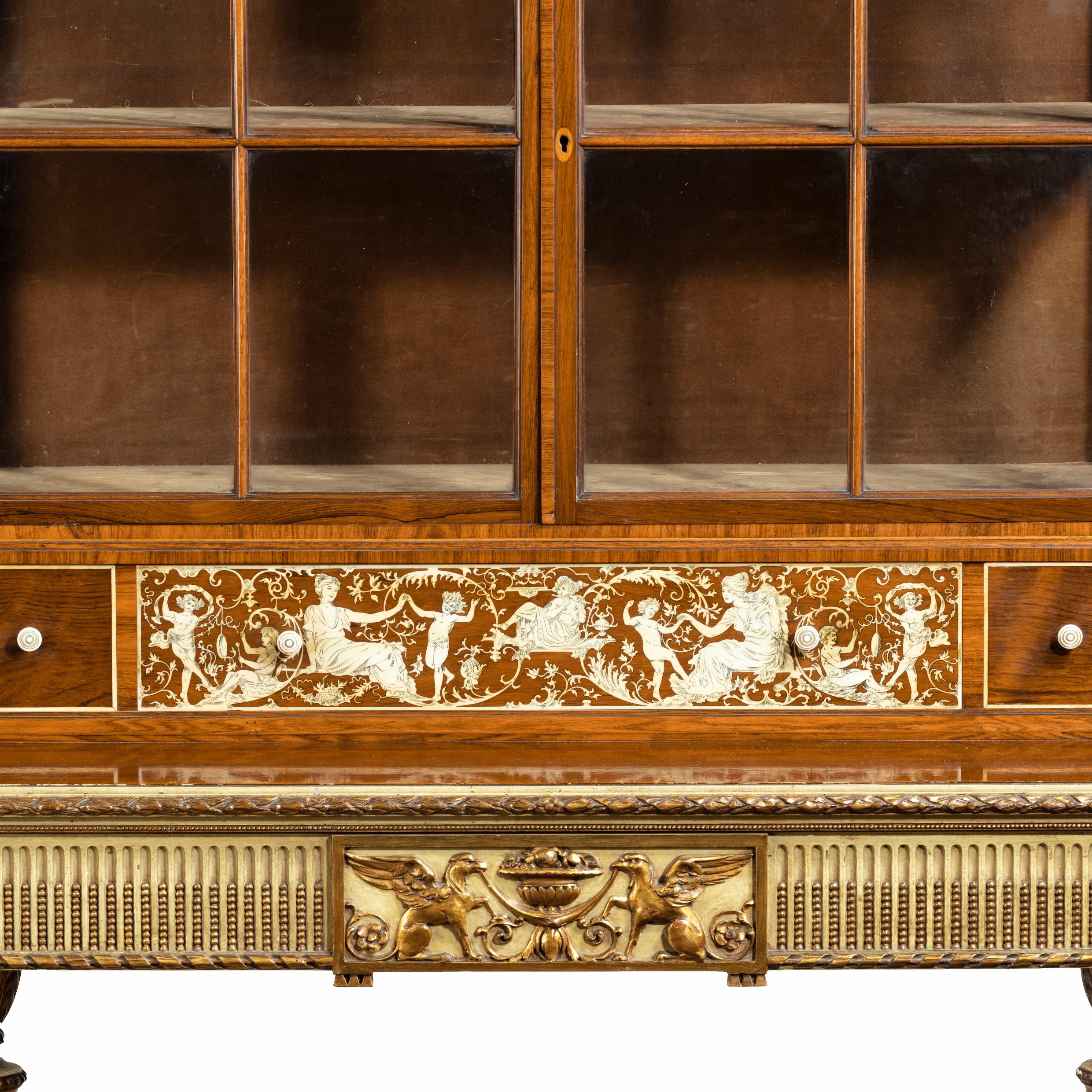 A drawing room cabinet by Collinson and Lock, the upper section in kingwood-banded rosewood with two glazed doors enclosing a shelf above a frieze with two small and one disguised drawer decorated with an ivory-inlaid panel showing dancing putti and