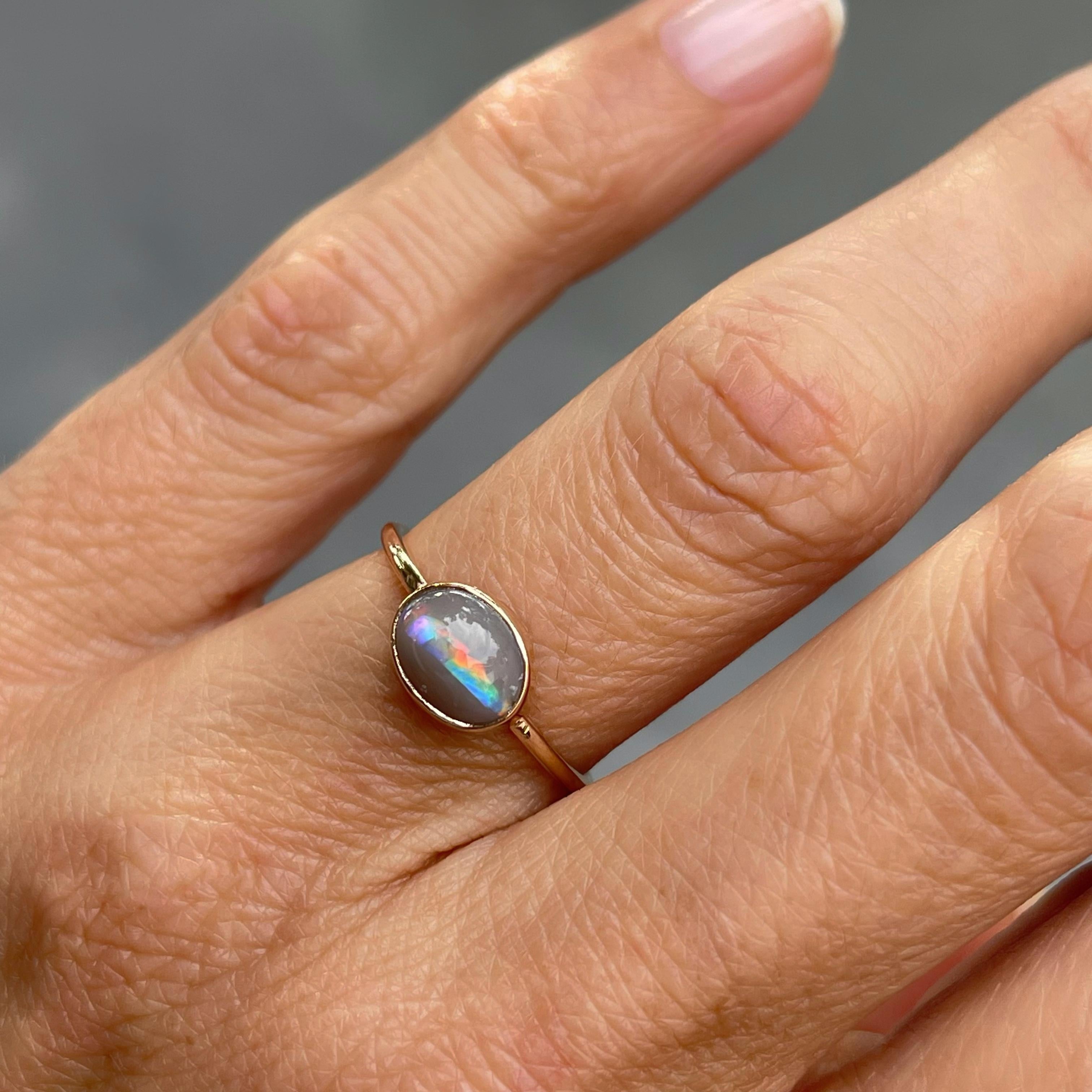 A streak of rainbow, pulsing with energy, dashes across the Dreamscape No. 13 Rose Gold Lightning Ridge Opal Ring.  The semi black opal has an opaque grey body tone with a racing stripe of pink, red, blue and green running horizontally across its