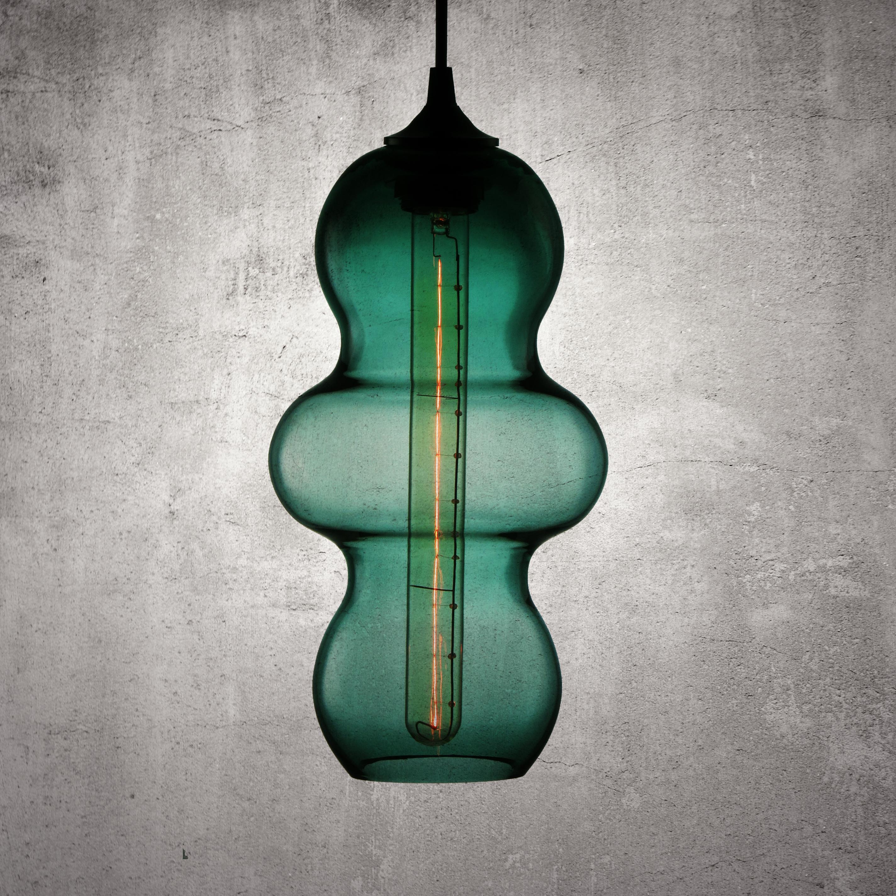 The Tamarindo contemporary glass pendant lamp is a contemporary interpretation of the tamarind fruit. Encapsulating its characteristics, the Tamarindo is sleek, curvaceous and light, hanging effortlessly with its long elongated form juxtaposed by a