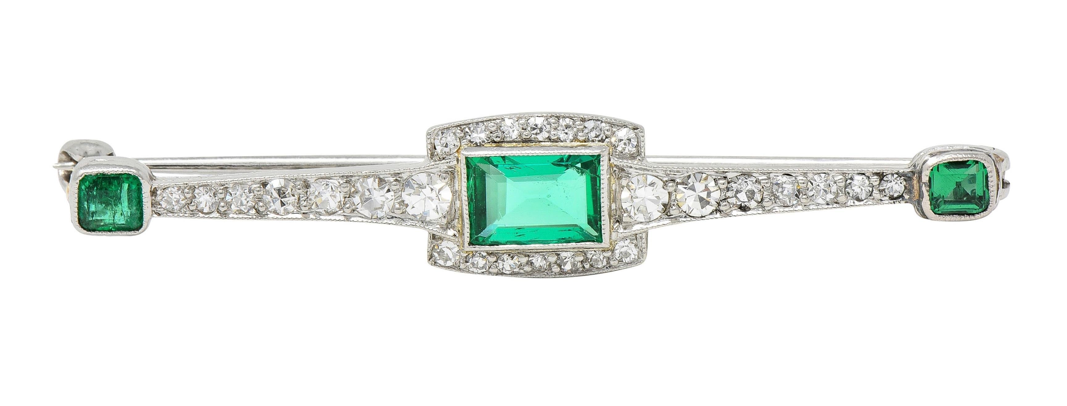 Designed as a tapered bar-style brooch centering a bezel set rectangular step-cut emerald 
Weighing approximately 0.79 carat - transparent medium green in color
With old single cut diamonds bead set as halo and throughout bar
Weighing approximately