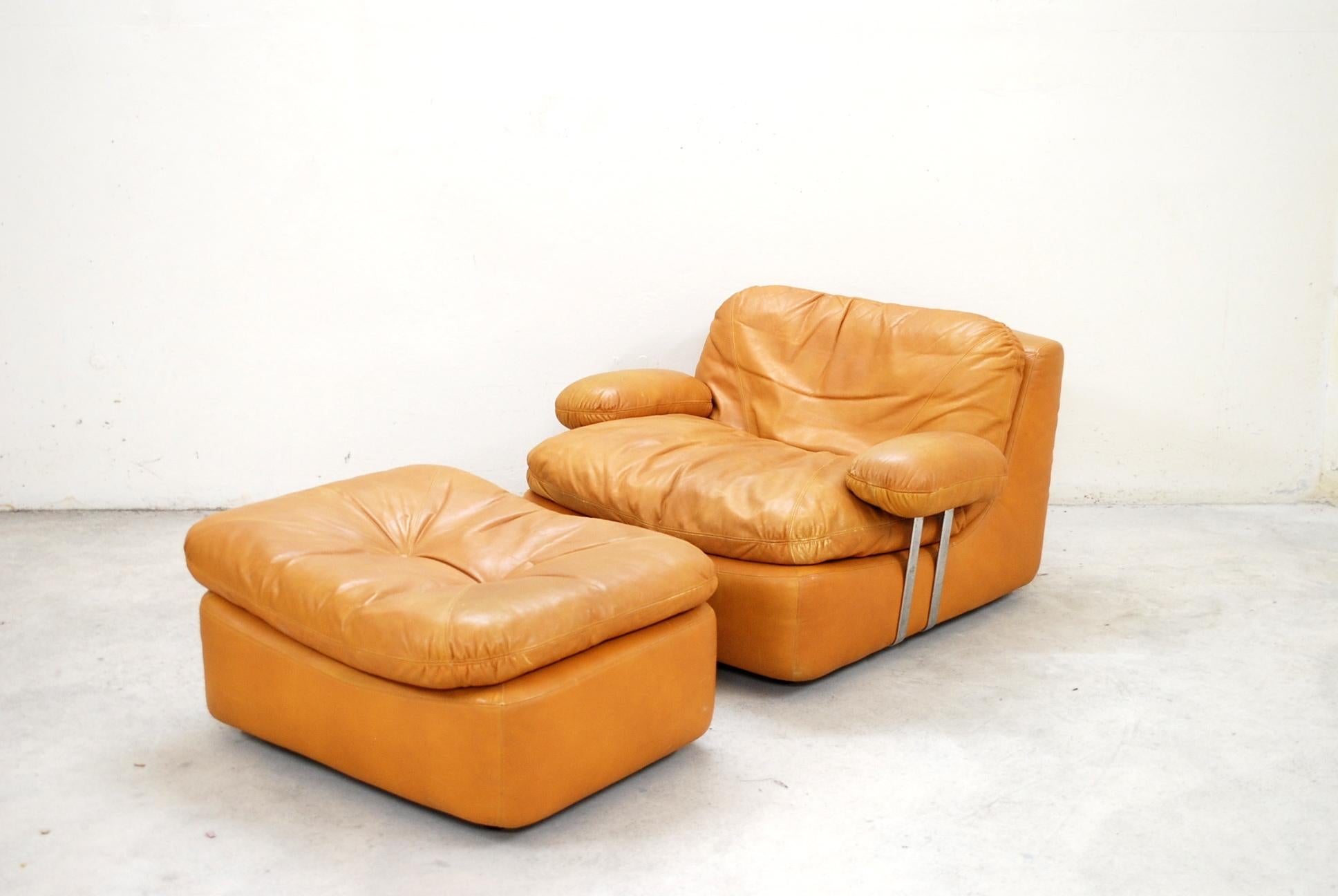 This lounge chair and ottoman were manufactured by Dreipunkt International and are upholstered in cognac colored semi-aniline leather. 
They feature black plastic feet, removable armrests with chromed metal sides and loose cushions filled with
