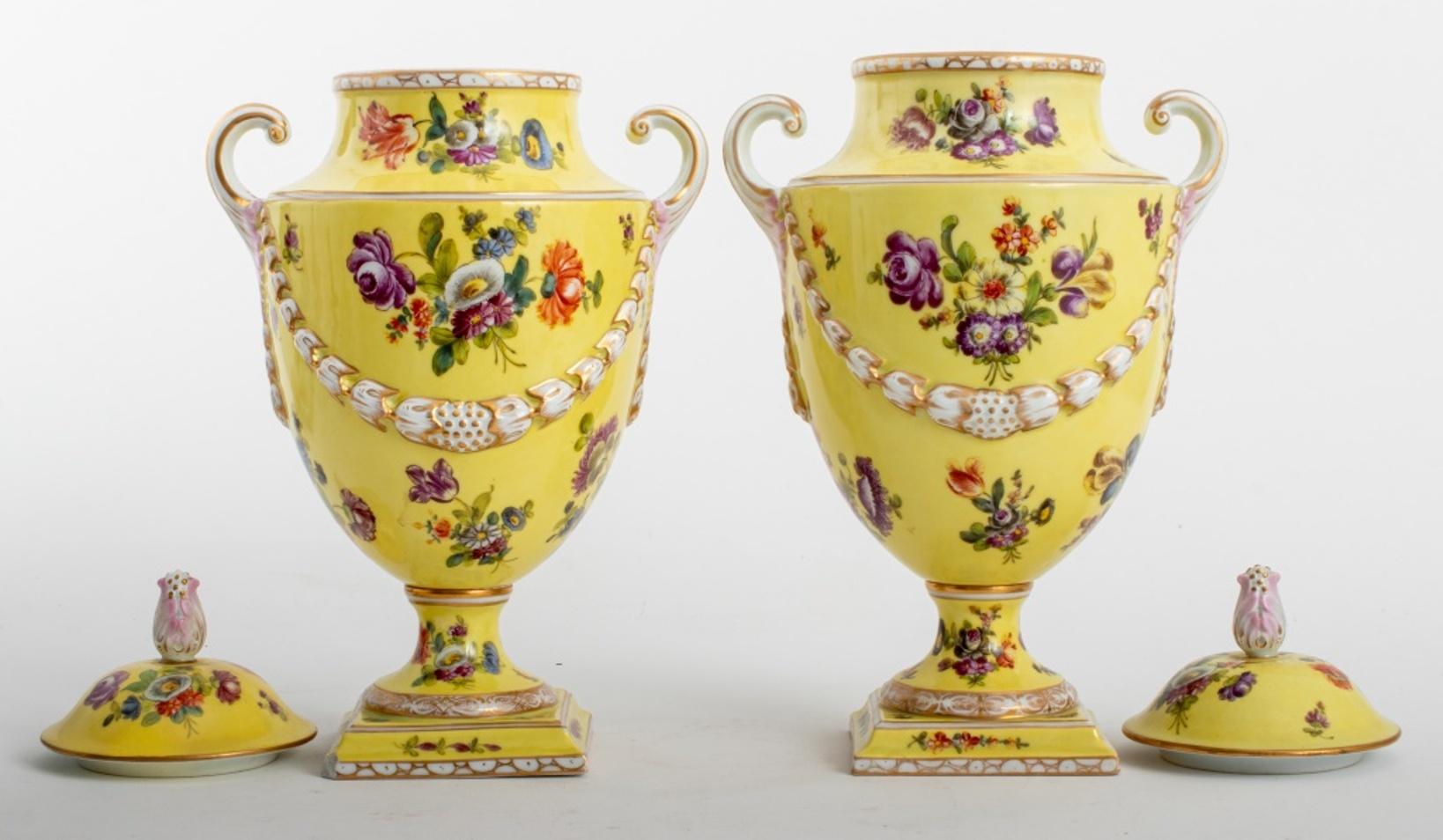Pair of Dresden German porcelain urn vases with lids, the ceramic vessels hand-painted with polychrome floral designs on yellow grounds with gilt accents, each with blue underglaze mark to underside. One with small chip to base.

Dimensions: 14.5