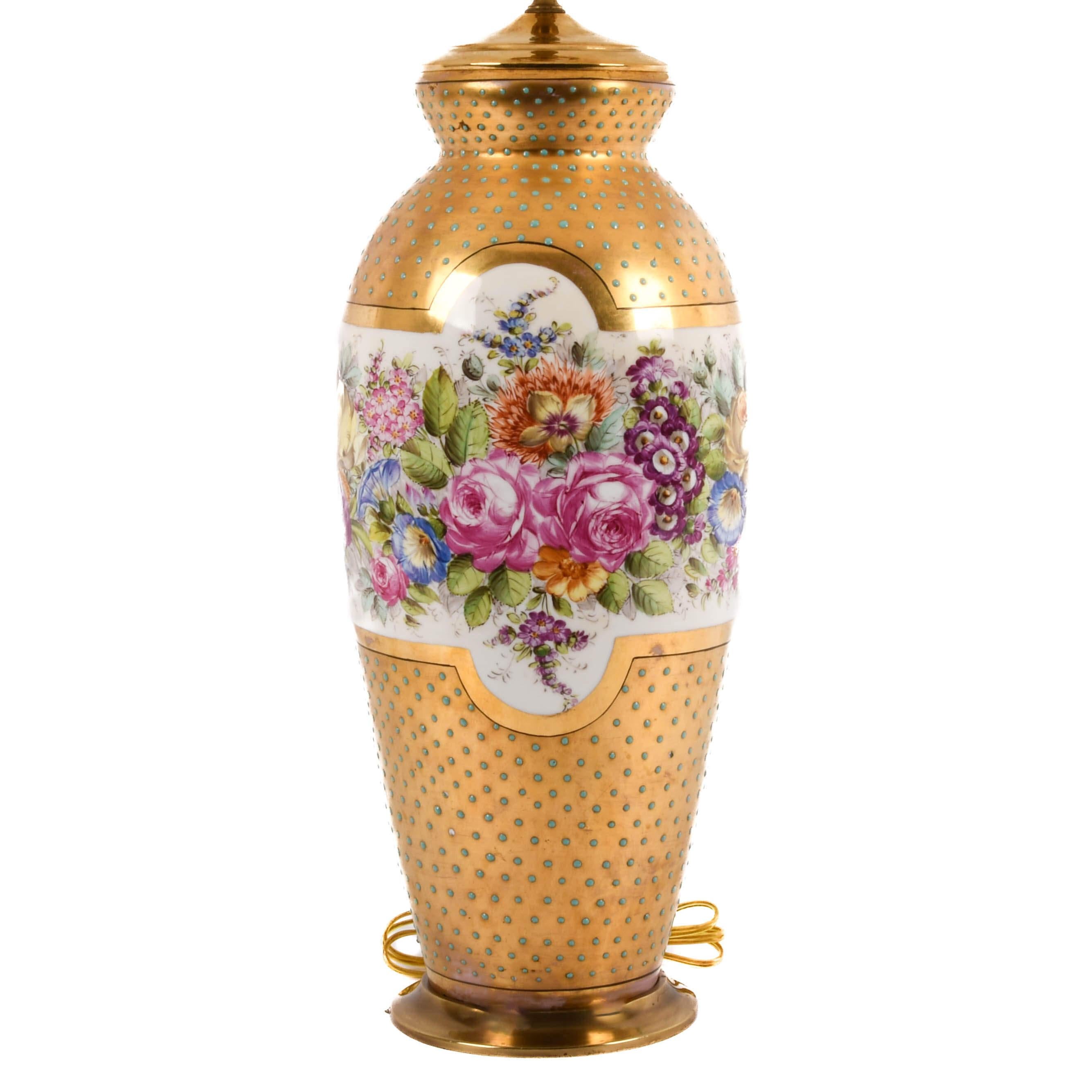Questa lampada floreale di Dresda, dipinta a mano, mostra una squisita miscela di arte e opulenza. La base presenta un sorprendente disegno di vivaci fiori dipinti a mano avvolti intorno a una fascia bianca, su uno sfondo d'oro scintillante ornato