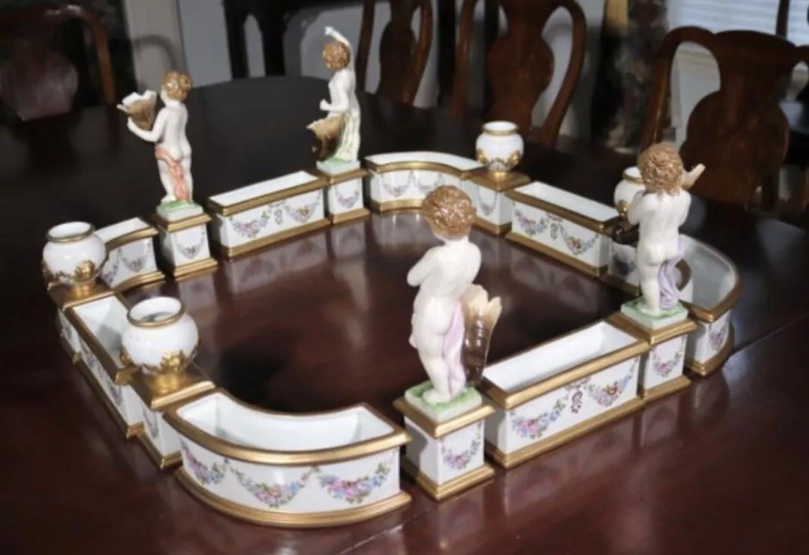 Dresden / Meissen Porcelain “surtout de table” centerpiece, having 16 pieces with

cherubs, cornucopia, urns and hand painted floral swags, the whole decorated with

floral swags, (4) urns and (4) putti with cornucopia. Marked in blue for the