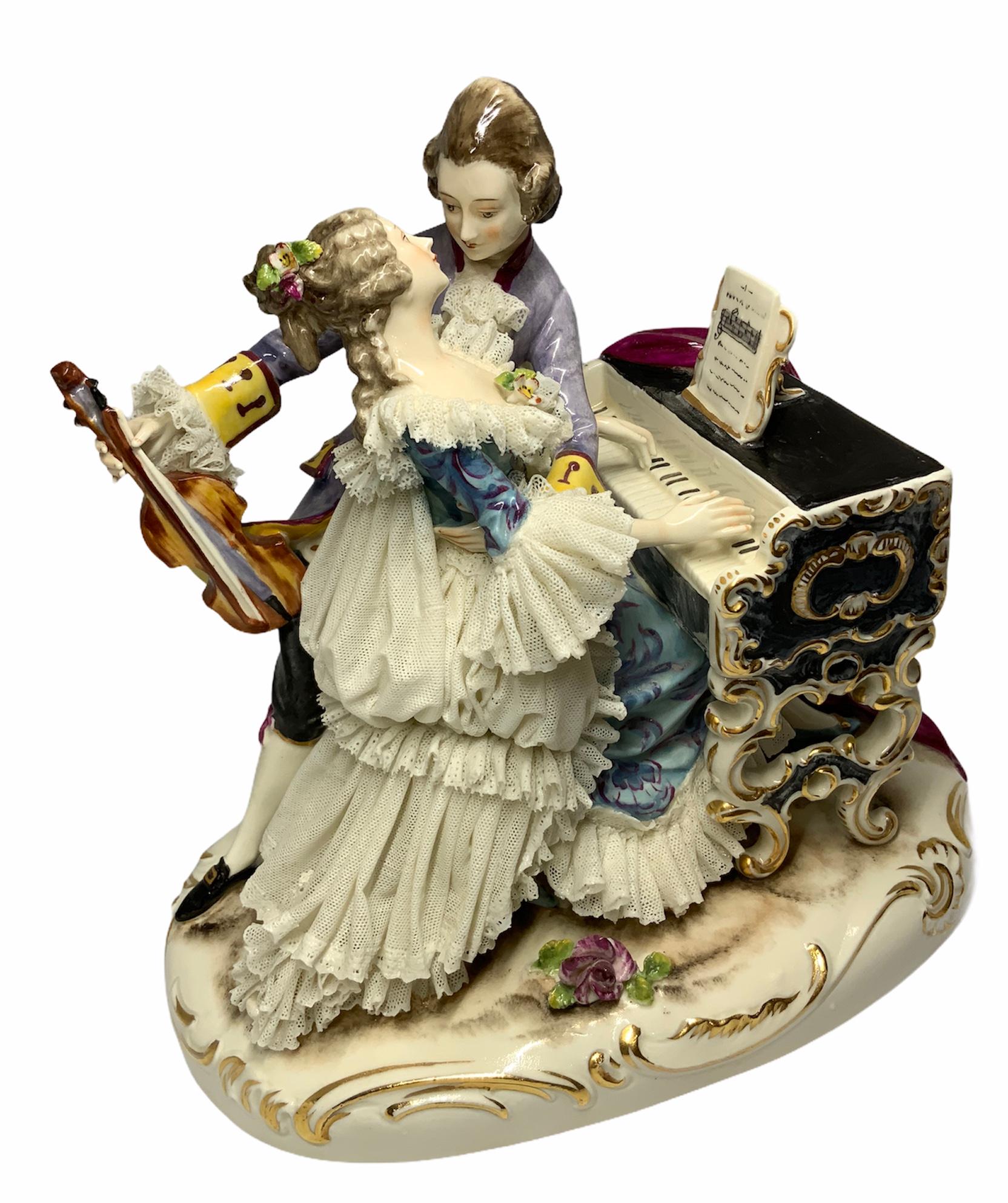 This is a Dresden Porcelain depicting a couple of musicians in love. She is playing the Louis XV style small black piano while he is holding the violin with his right hand and embracing her with the left arm, almost ready to kiss her. Both of them