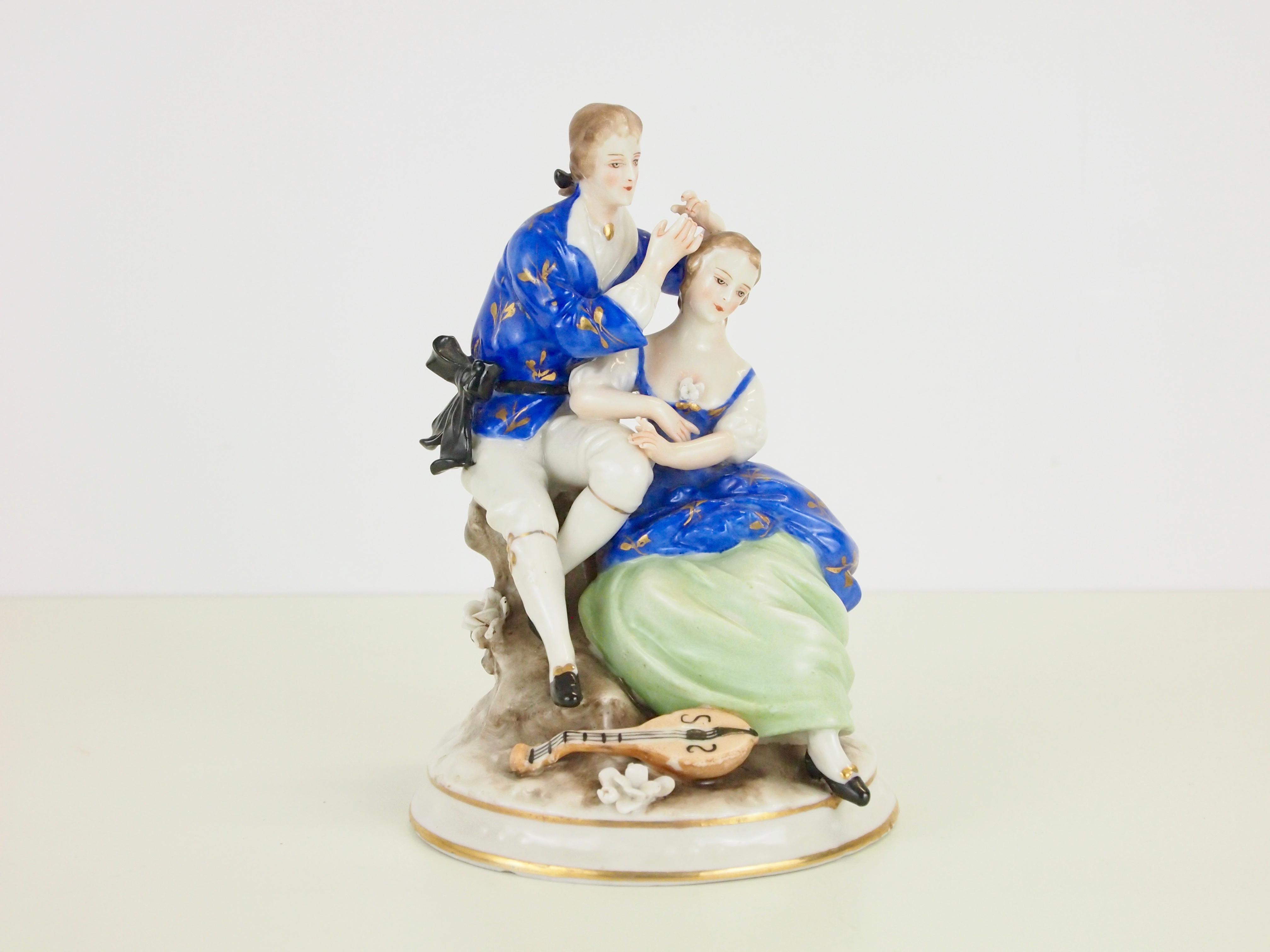 An antique/midcentury fine porcelain hand painted statuette depicting a romantic Classic couple.

Lovely high quality fine porcelain statuette made by the Saxon Porzellan manufacturer Ackermann & Fritze. It has very fine hand painted details and