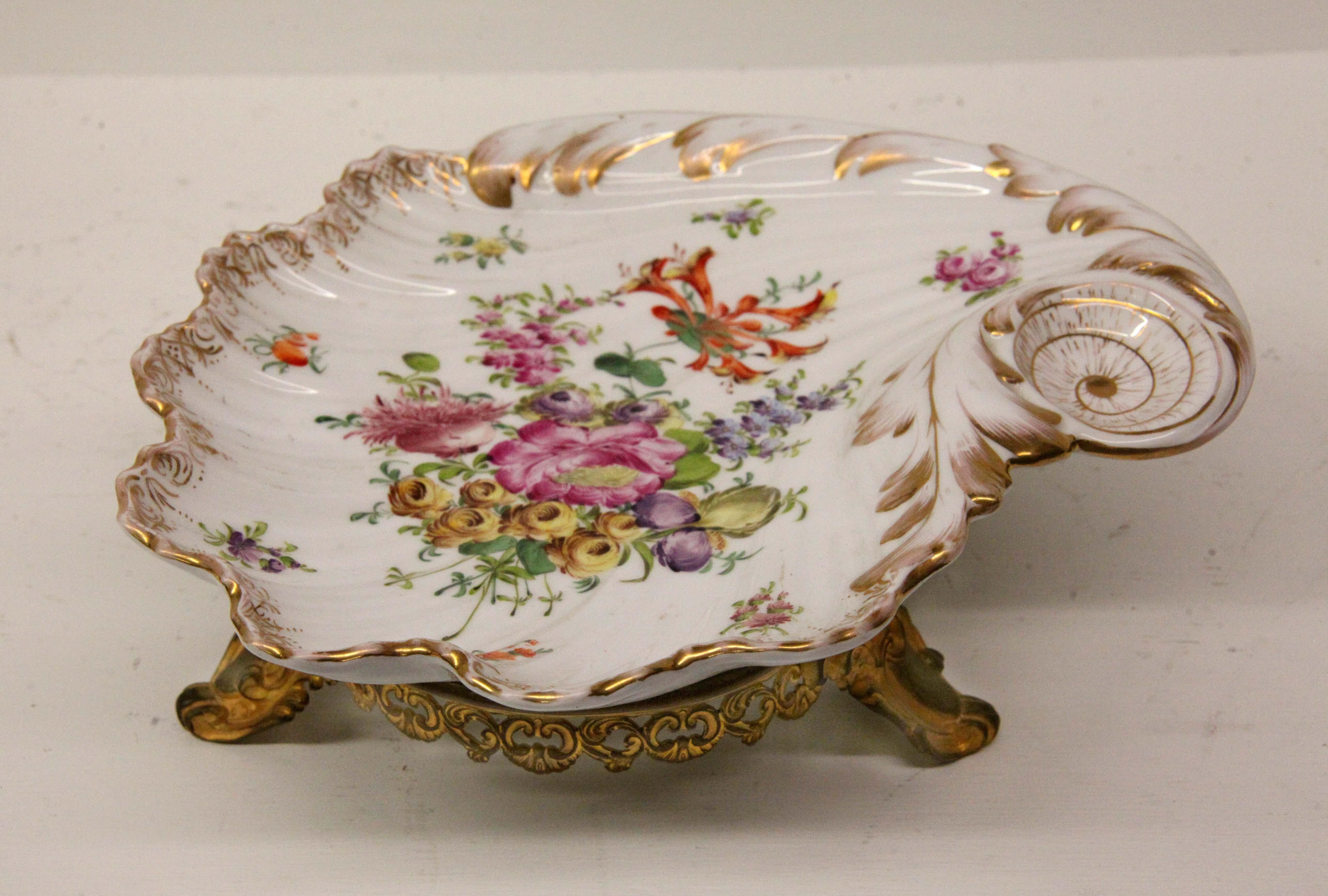 Dresden serving dish with gilt base, with scalloped edge and shallow well surrounding the center of flowers and foliate work, the attached gilt brass base with intricately reticulated apron and scroll feet.