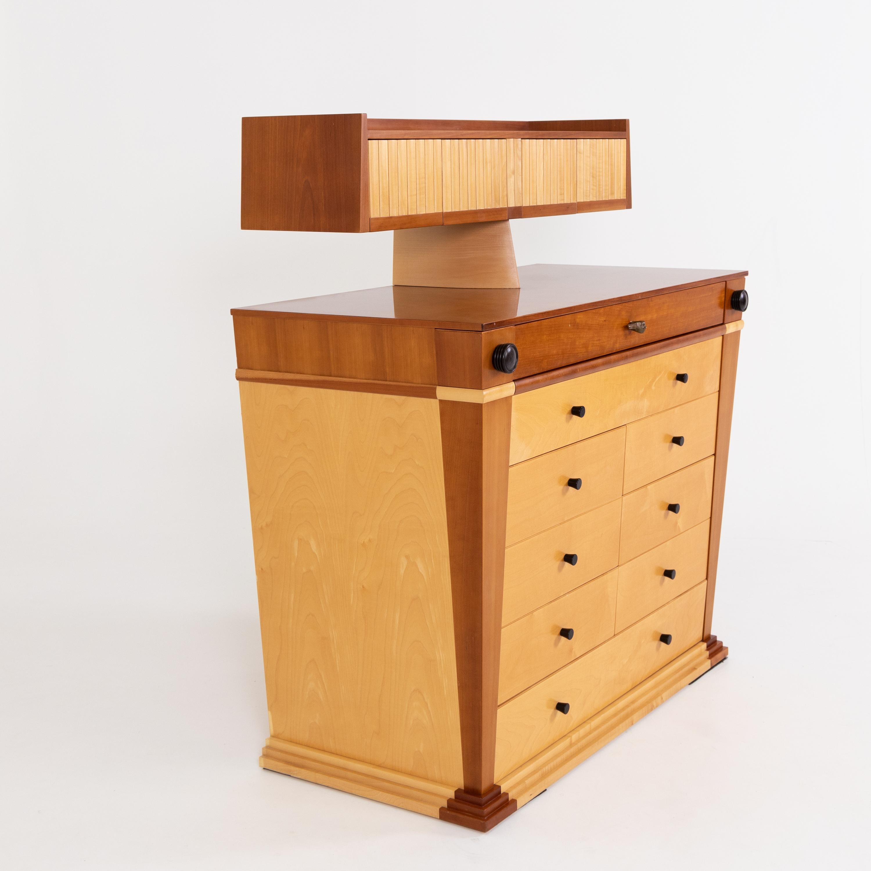 Chest of drawers designed by Massimo Scolari for Giorgetti. The chest of drawers stands on a stepped base with a total of nine drawers and a top with further compartments. Mask-shaped bronze knob on the top drawer and side pull-out compartments with