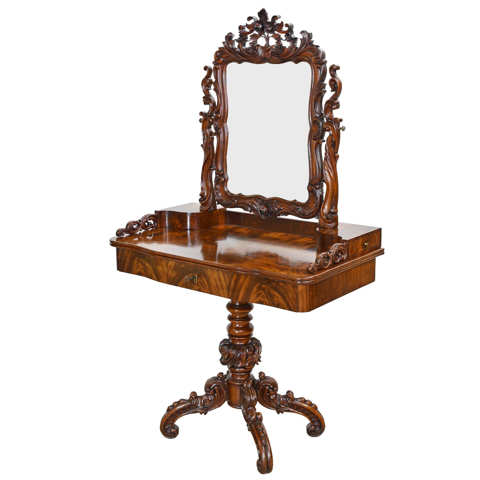 An exquisite Karl Johan dressing table or vanity in fine West Indies mahogany with elaborate floral and foliate rococo carvings along the mirror frame and center pedestal base. Offers a drawer on each side, and a center drawer on the apron. Comes