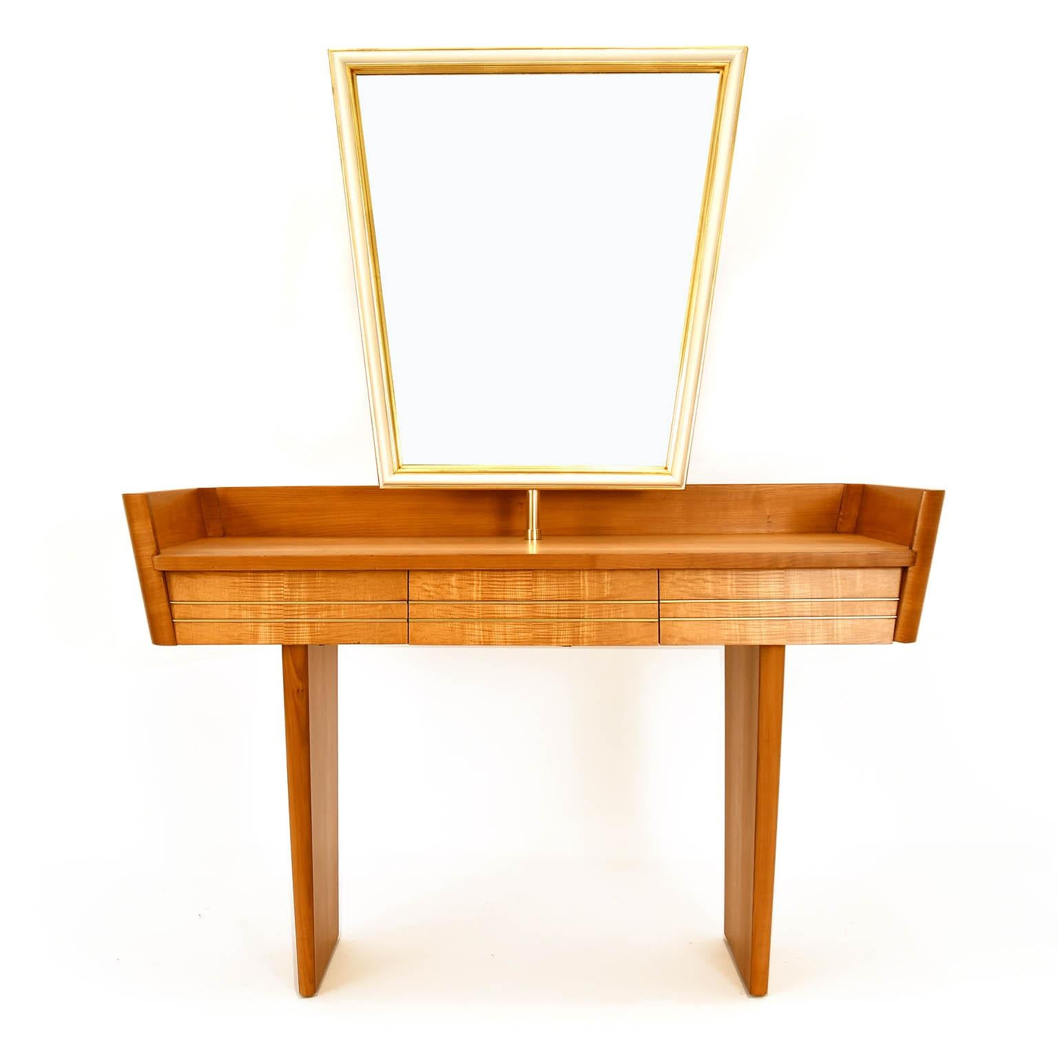 Midcentury dressing table made in Austria. The frame is made of solid cherrywood and softwood with cherry veneer. The three drawers have metall inlays made of brass. The mirrow's frame is partly lacquered in gold and creme color. A brass
