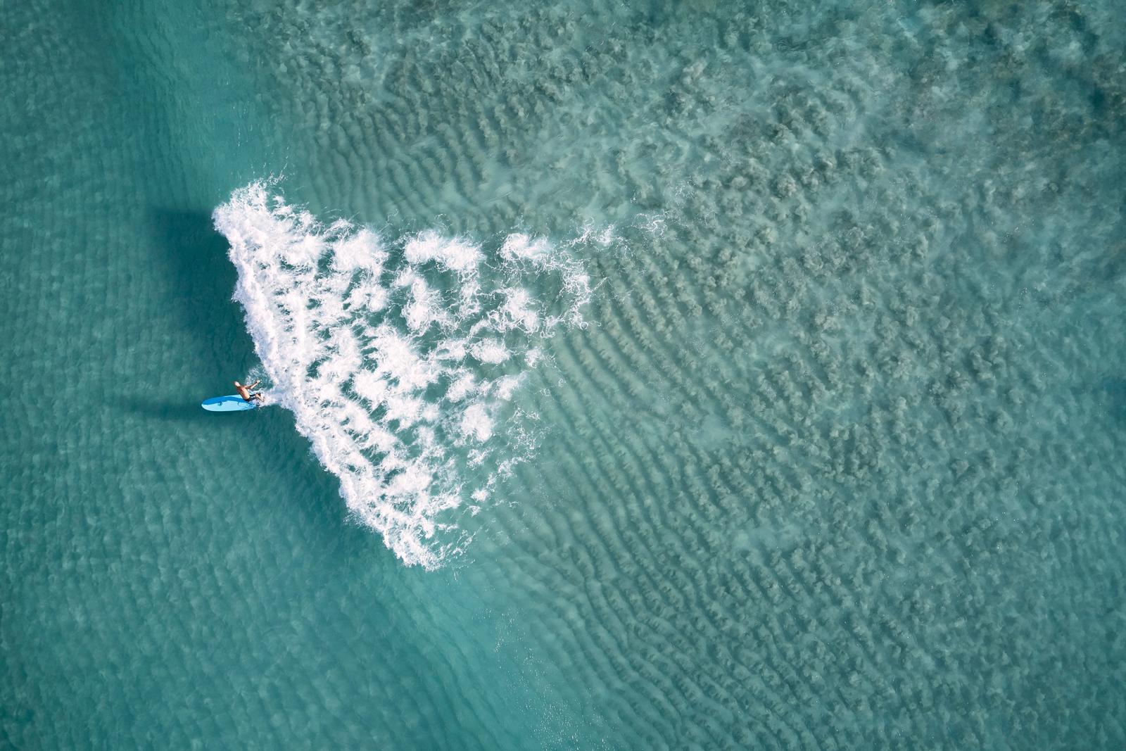 Image aérienne en couleurs d'un surfeur surfant sur une vague à bord d'un longboard. - Photograph de Drew Doggett