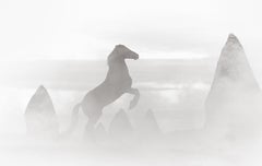 Un cavallo nero che si erge con il fumo che si alza e i pinnacoli di roccia sullo sfondo.