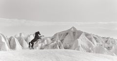 Un cheval foncé descendant avec des formations de pierres et des nuages bas en arrière-plan