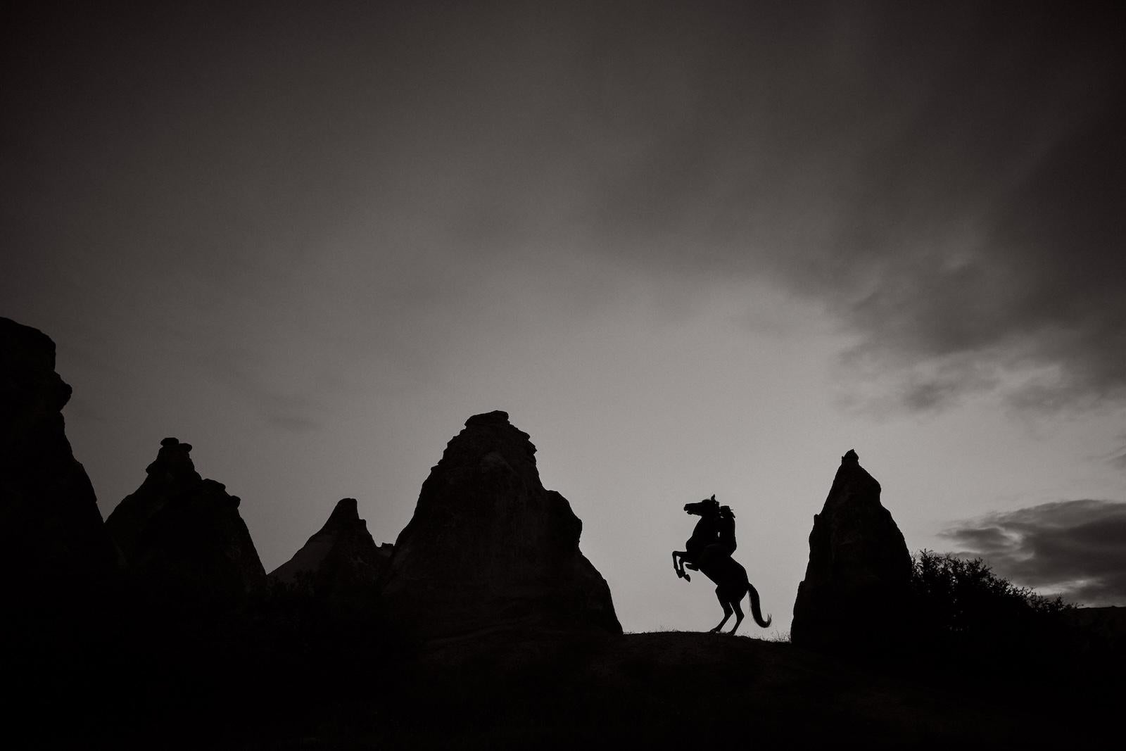 Un caballo se encabrita, silueteado contra el cielo que se oscurece y las formaciones rocosas - Photograph de Drew Doggett