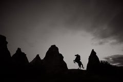 A horse rears up, silhouetted against the darkening sky and rock formations