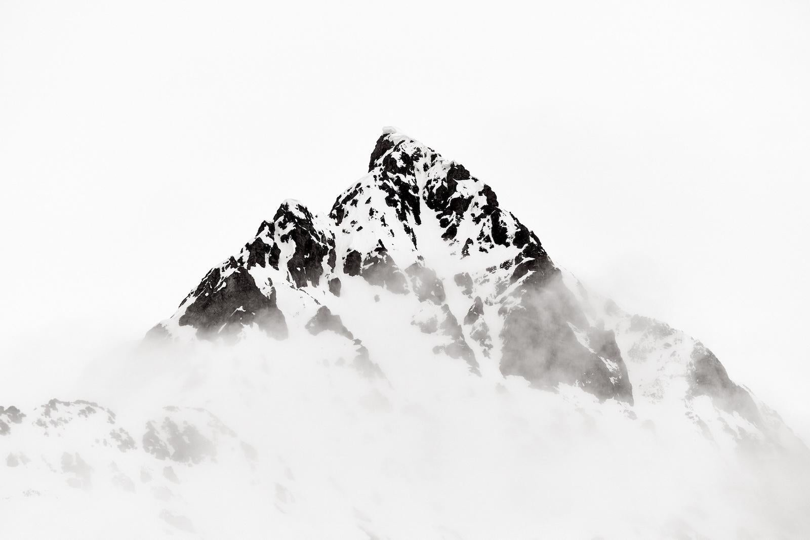 A lone snowy peak rising above the clouds and mist with a flat white minimal nat - Photograph by Drew Doggett