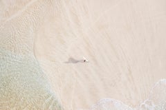 Un surfista solitario si trova sulla sabbia con la sua tavola mentre l'acqua gli lambisce i piedi