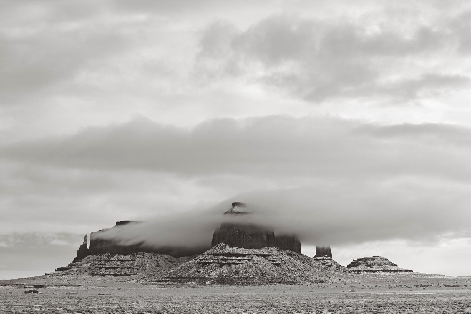 Drew Doggett Black and White Photograph - Clouds around a rock formation in Monument Valley, Utah